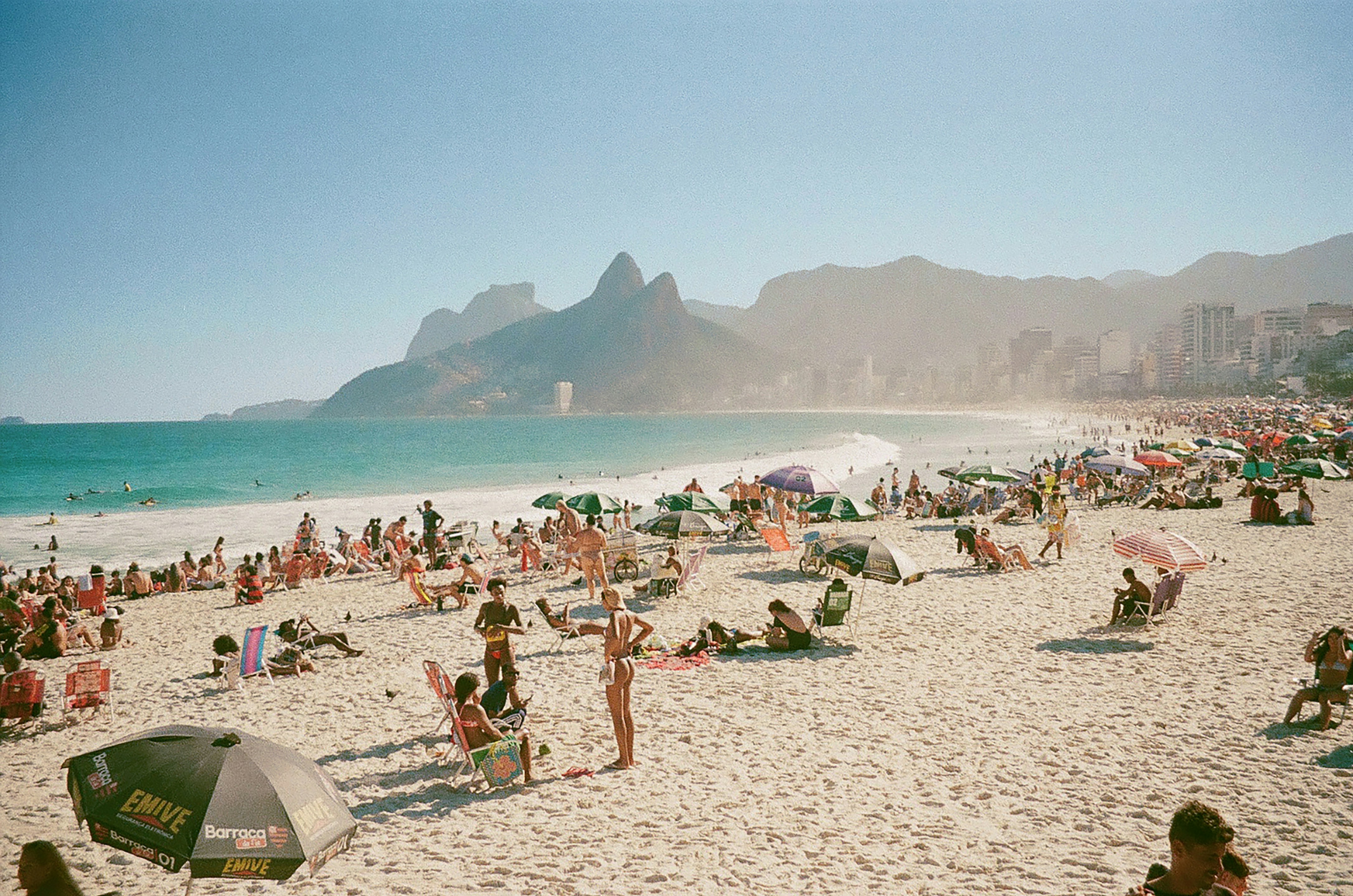 Menschen am Ipanema-Strand mit den Dois Irmãos-Bergen im Hintergrund in Rio de Janeiro