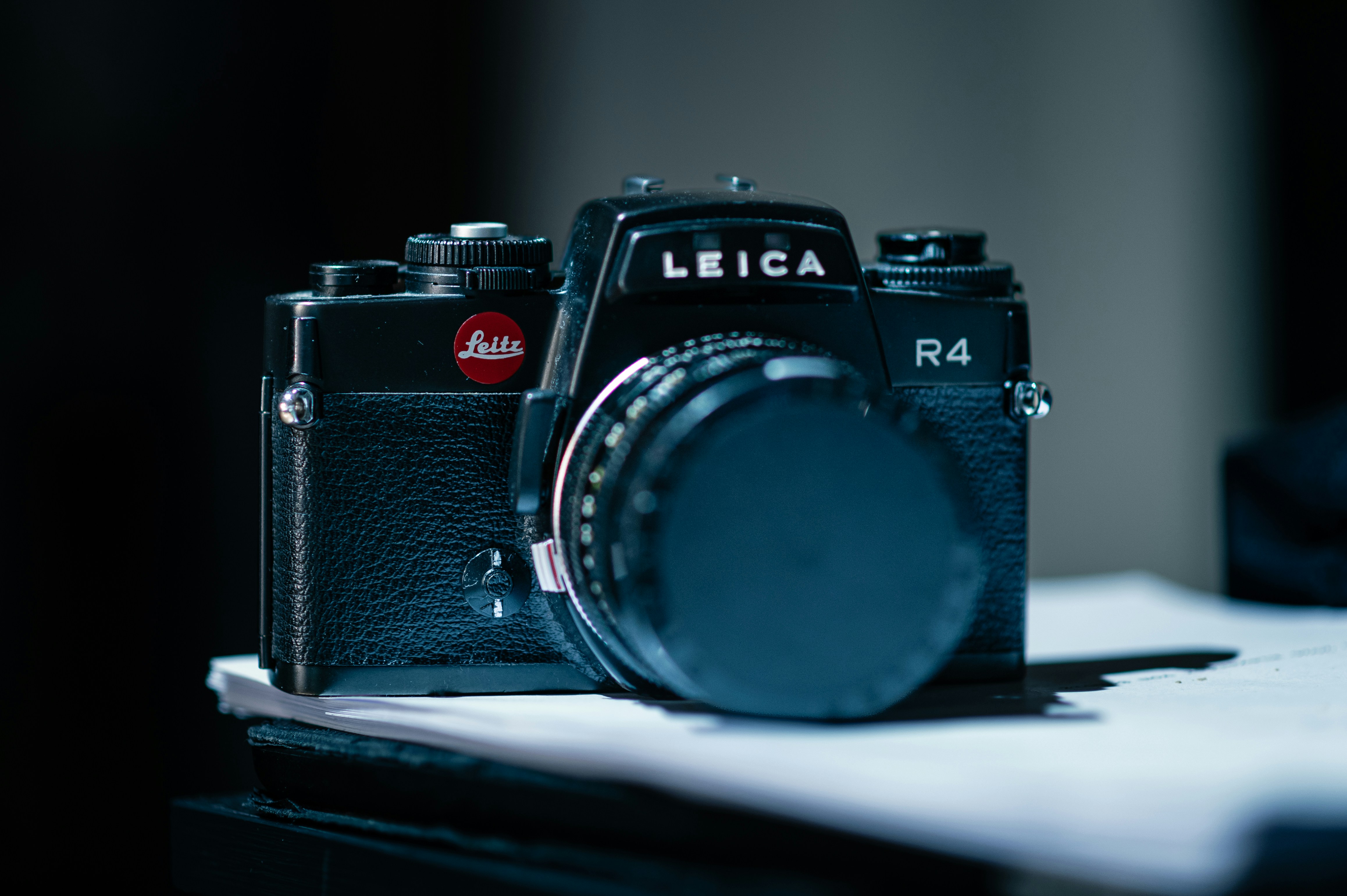 A black Leica R4 film camera with a lens cap on a white surface