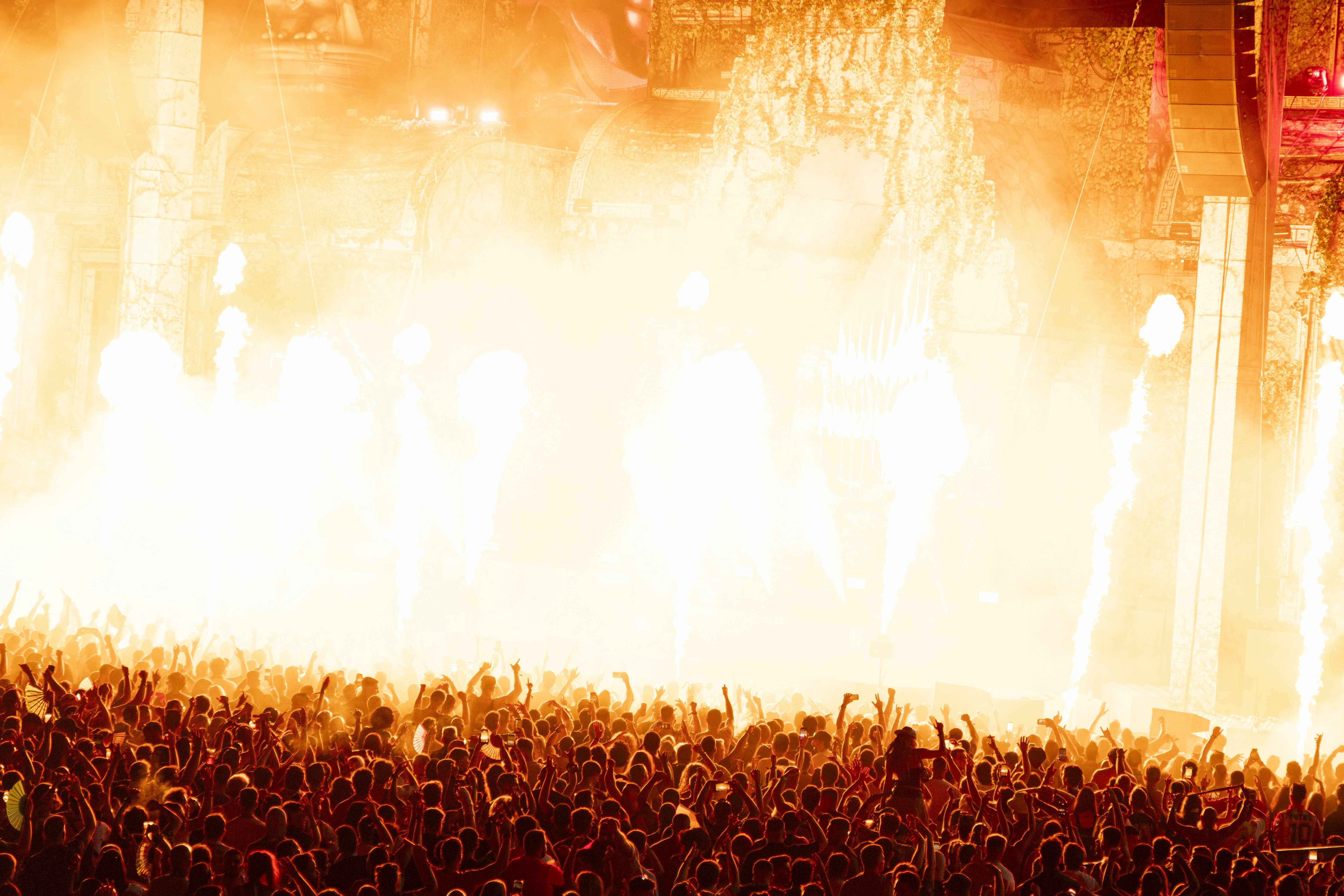 A crowd of people at a concert with bright orange stage lights and pyrotechnics