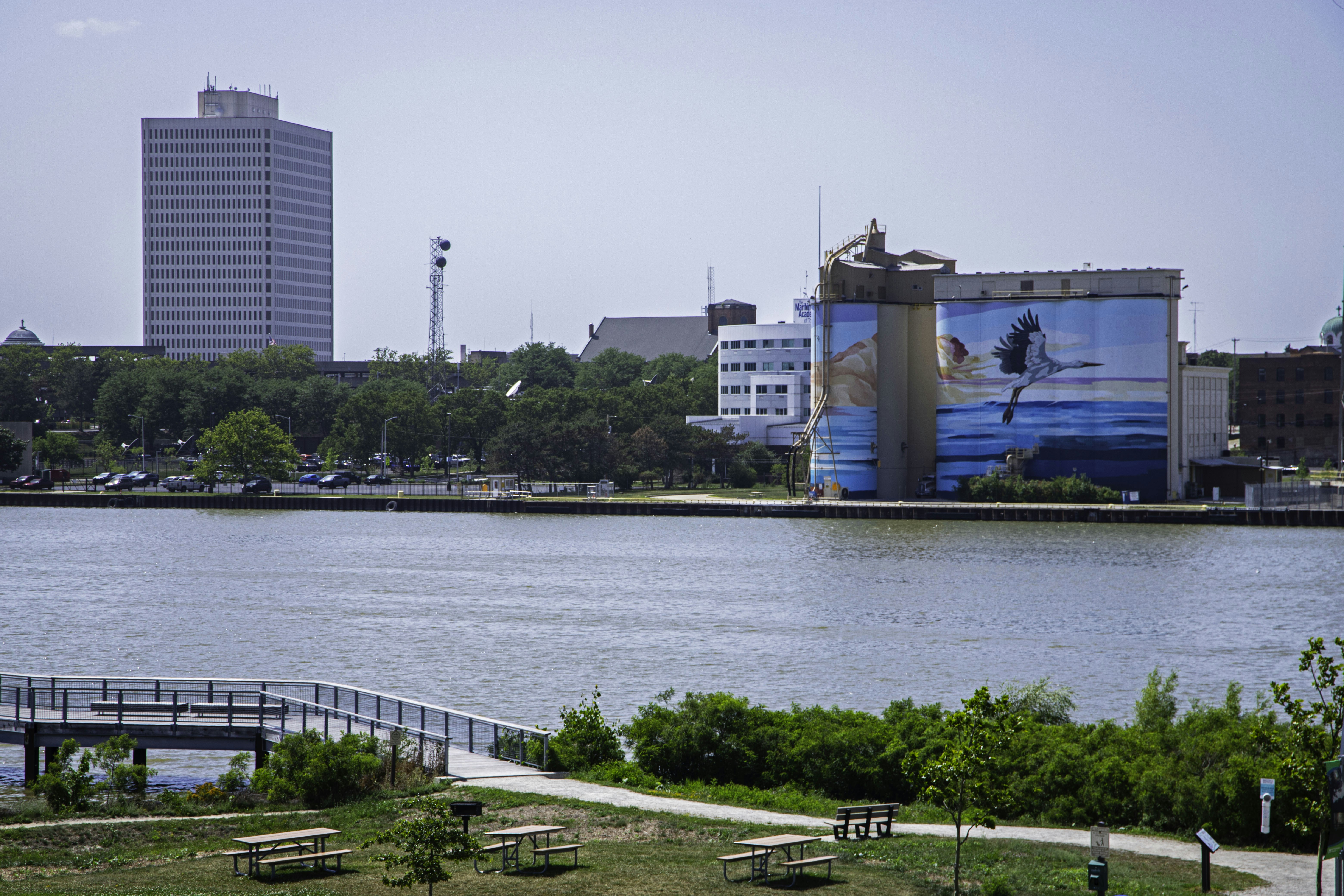 A riverfront park with picnic tables and a mural on industrial grain silos