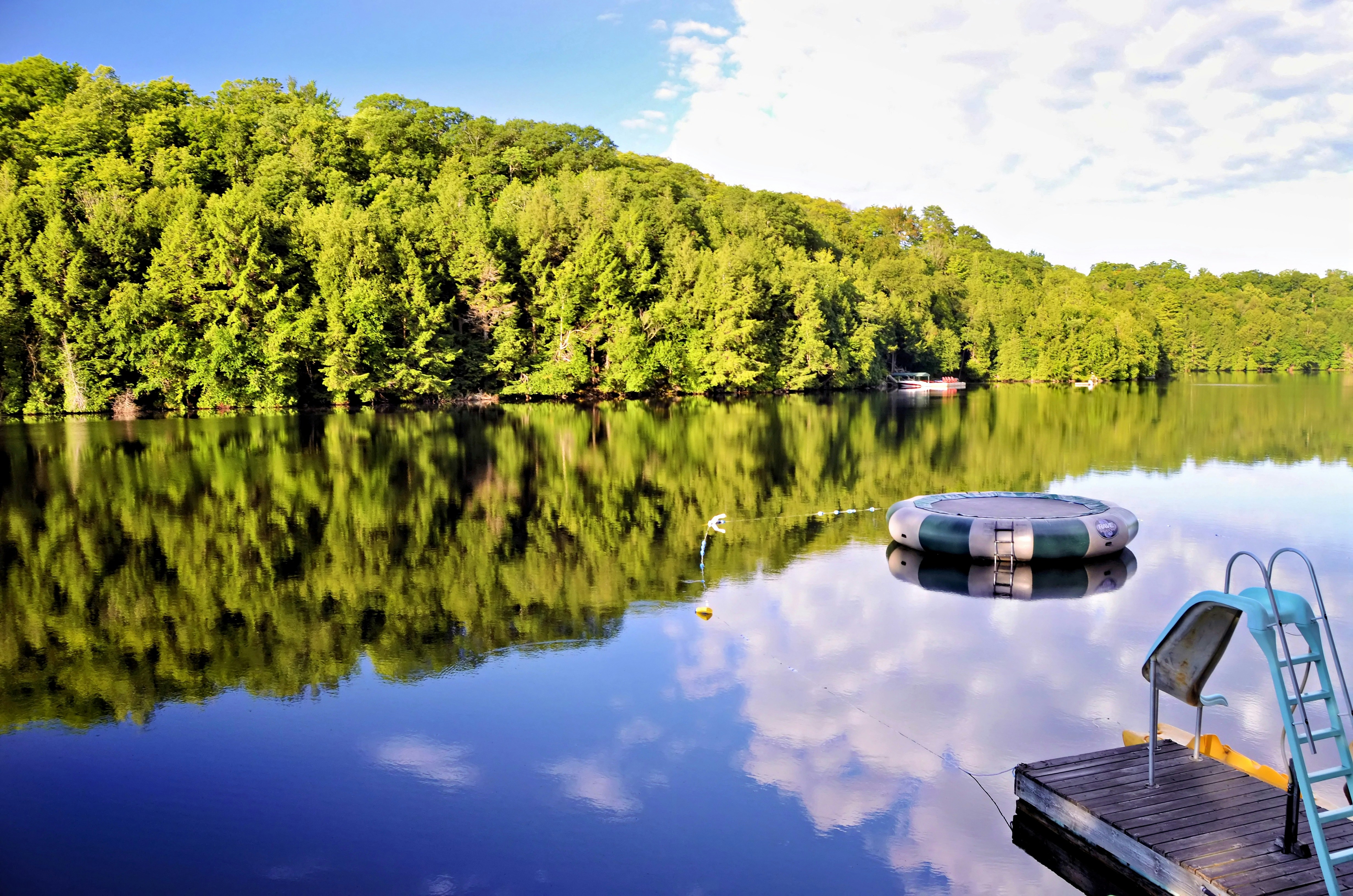 A floating trampoline and a wooden dock with a slide on a calm lake