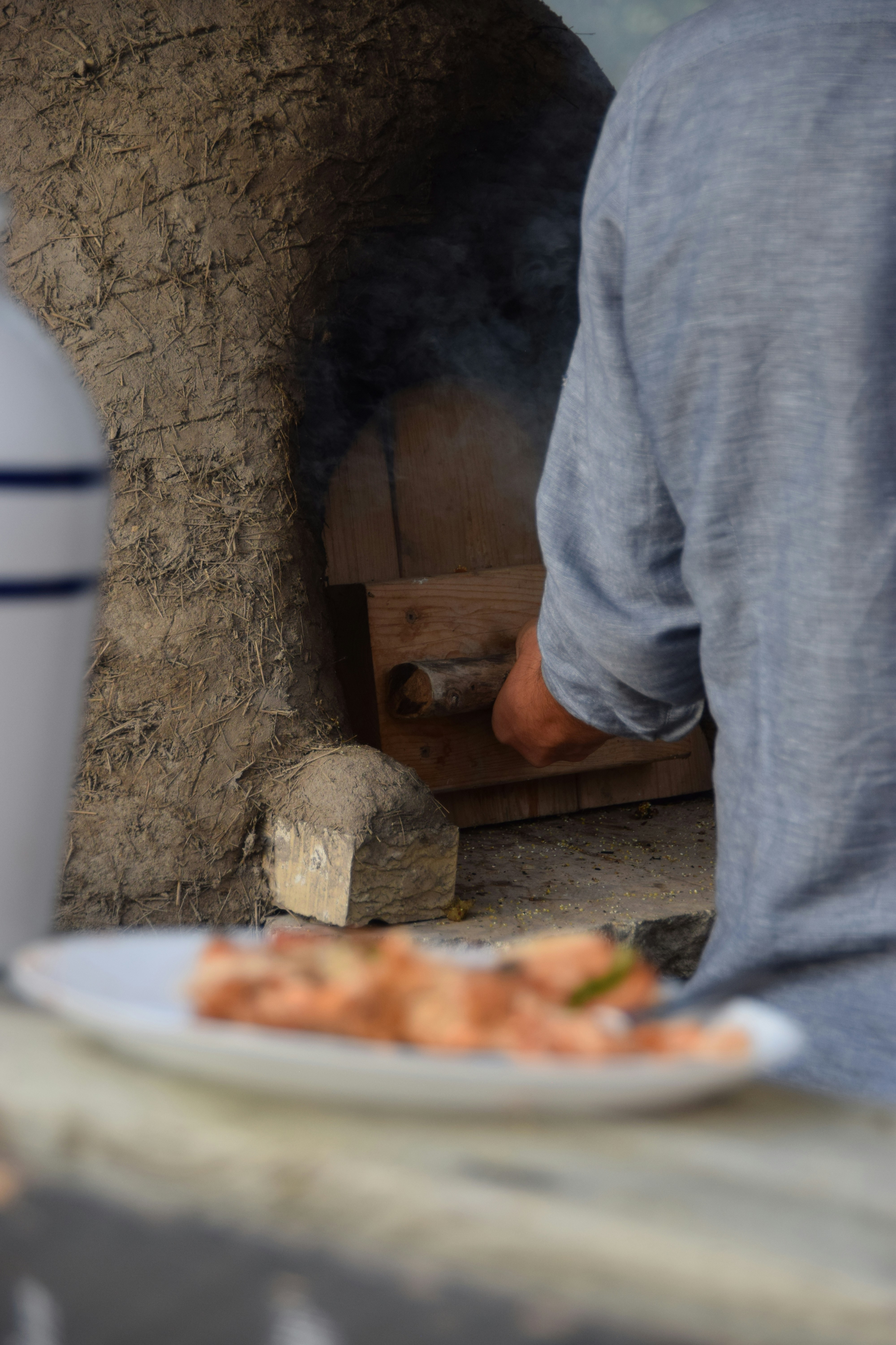 A person in a blue shirt using a wooden tool in a clay oven