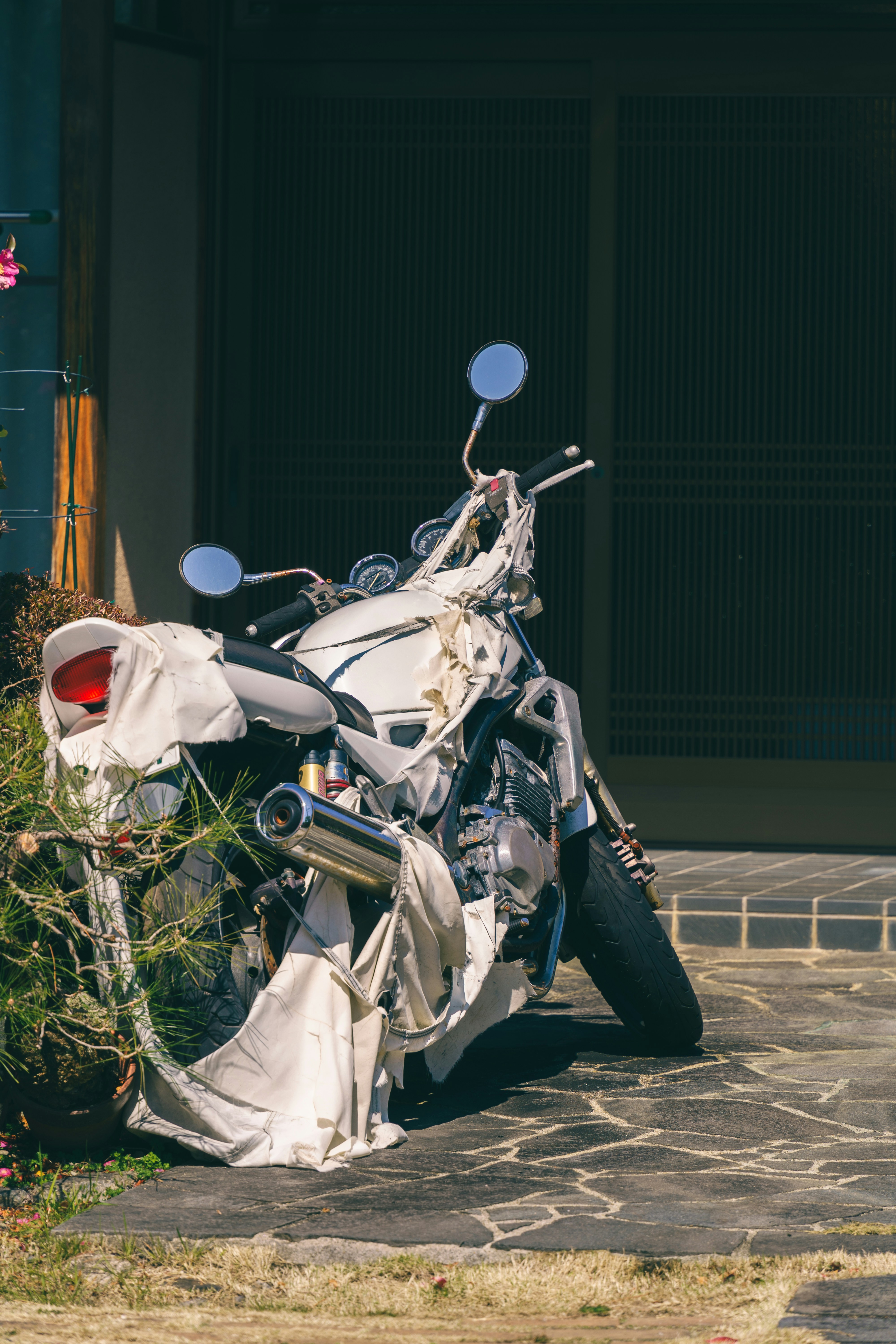 A white motorcycle covered in torn fabric strips on a stone patio