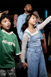 A boy and a girl holding hands with eyes closed in a crowd