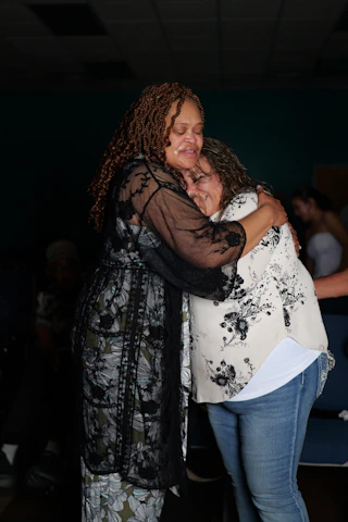 Two women embracing in a tight hug, both with eyes closed and tearful expressions
