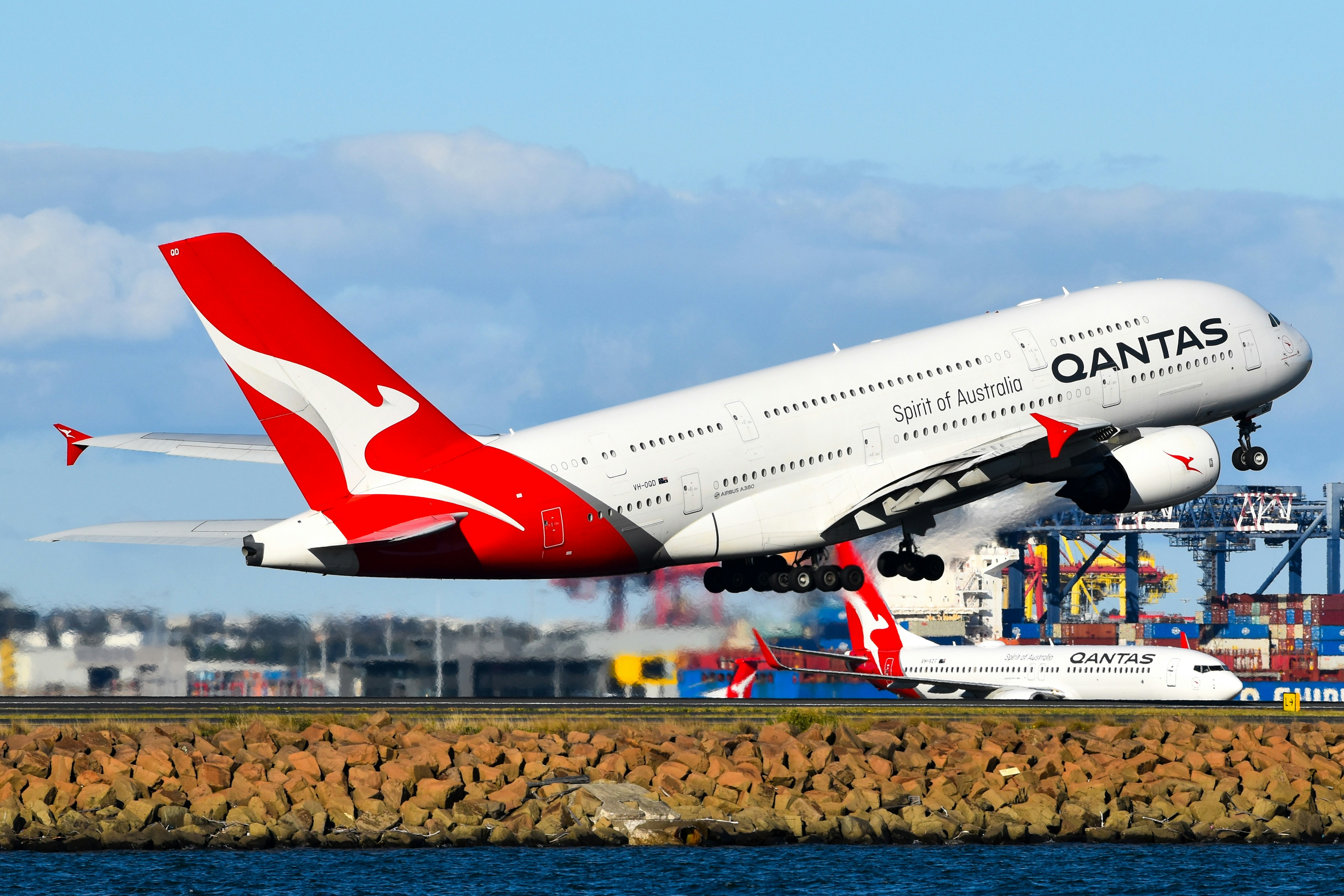 A Qantas Airbus A380 taking off from a runway near a shipping port