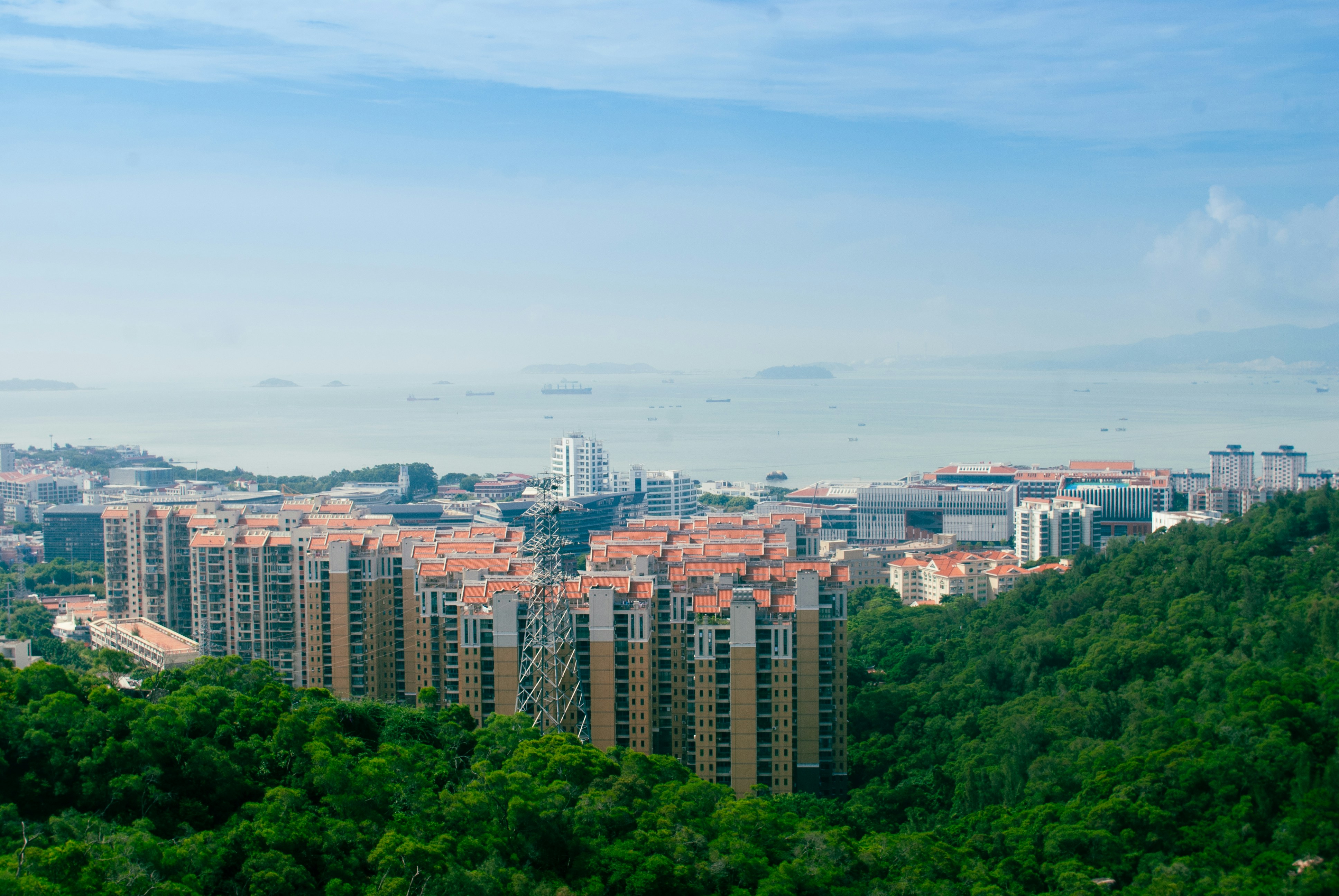 High-rise apartment buildings with orange roofs nestled in a lush green forest by the sea