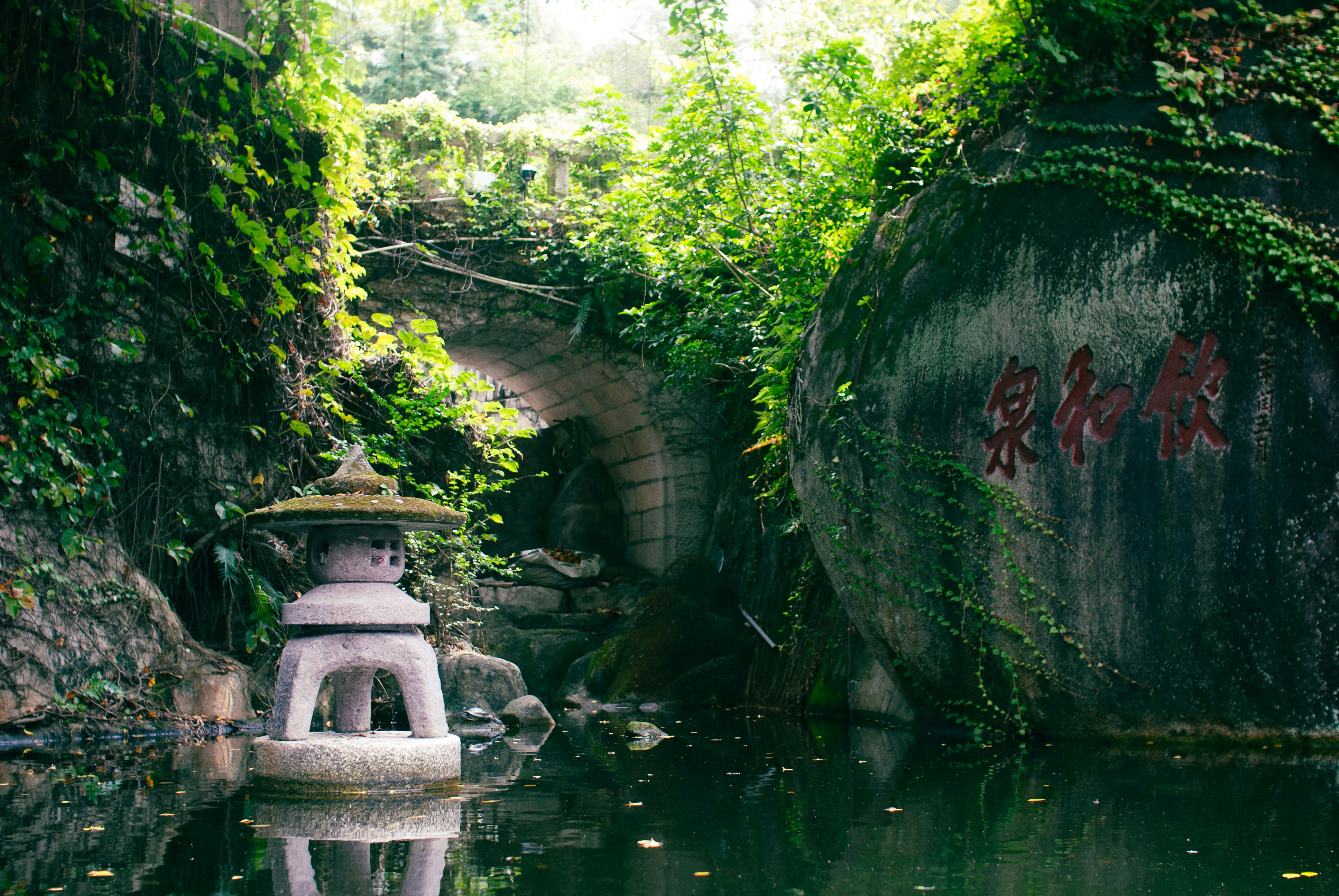 A stone lantern in a pond beside a large boulder with red carved characters