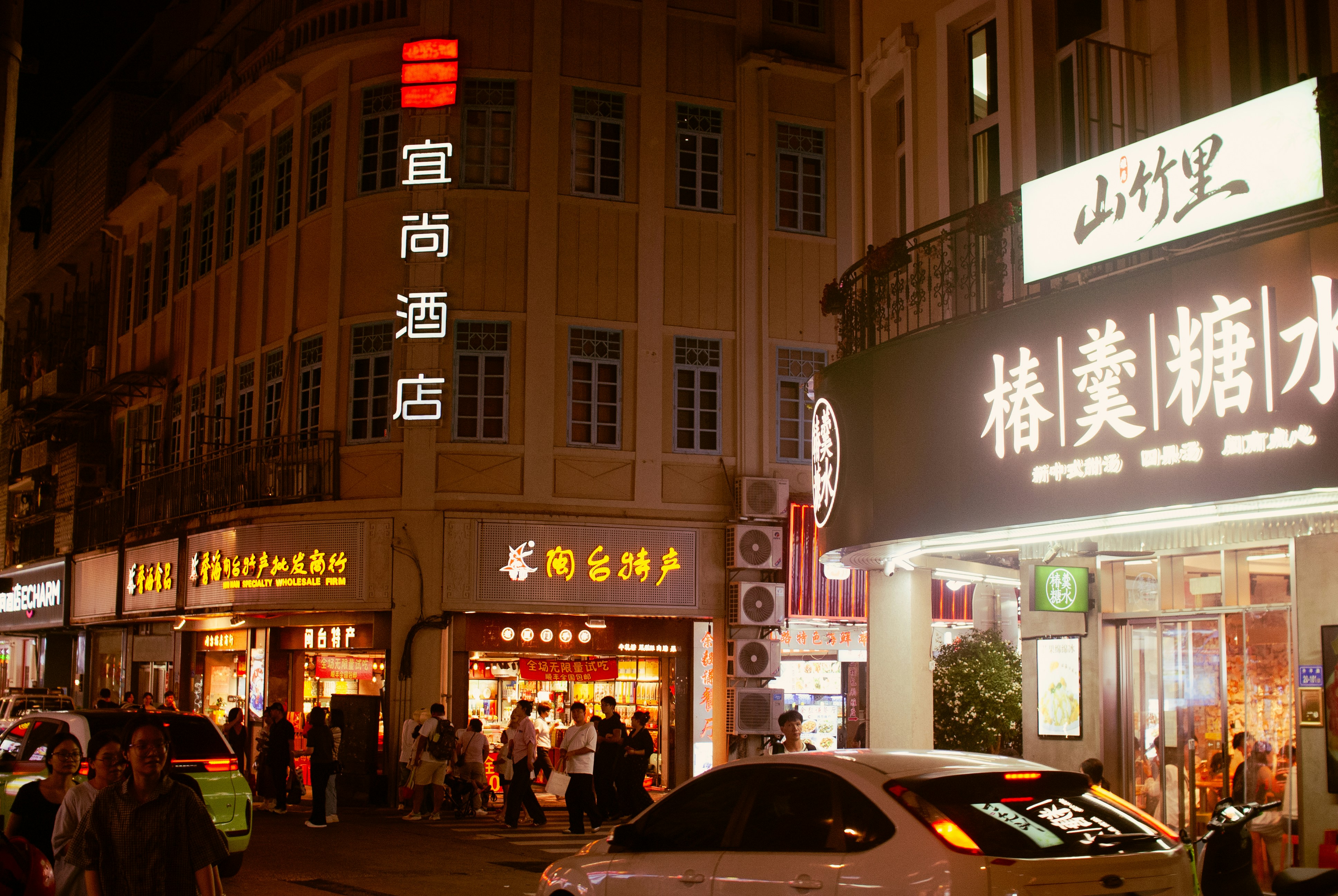 People walking on a busy street at night with illuminated shop signs