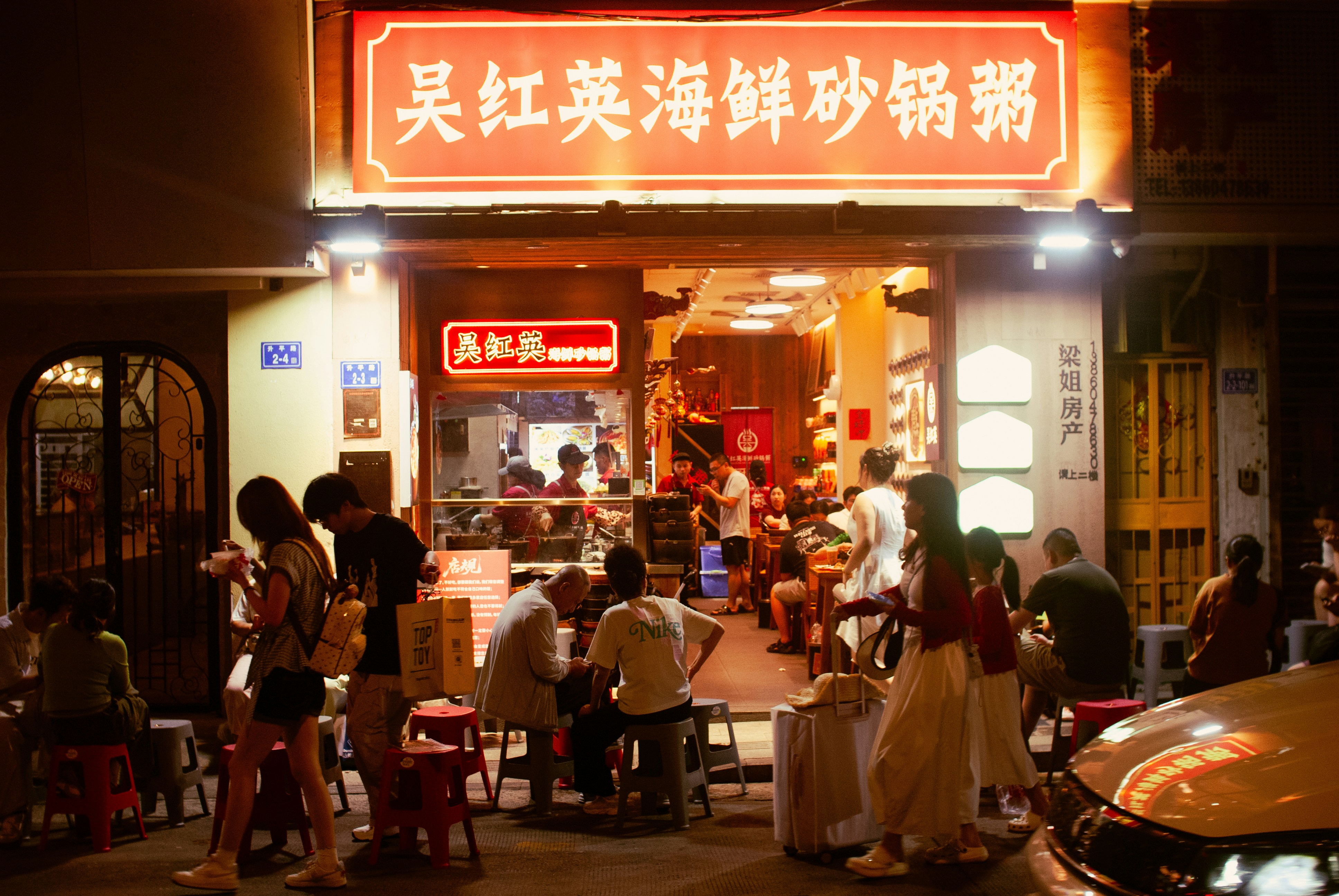 People dining at small tables outside a brightly lit restaurant at night