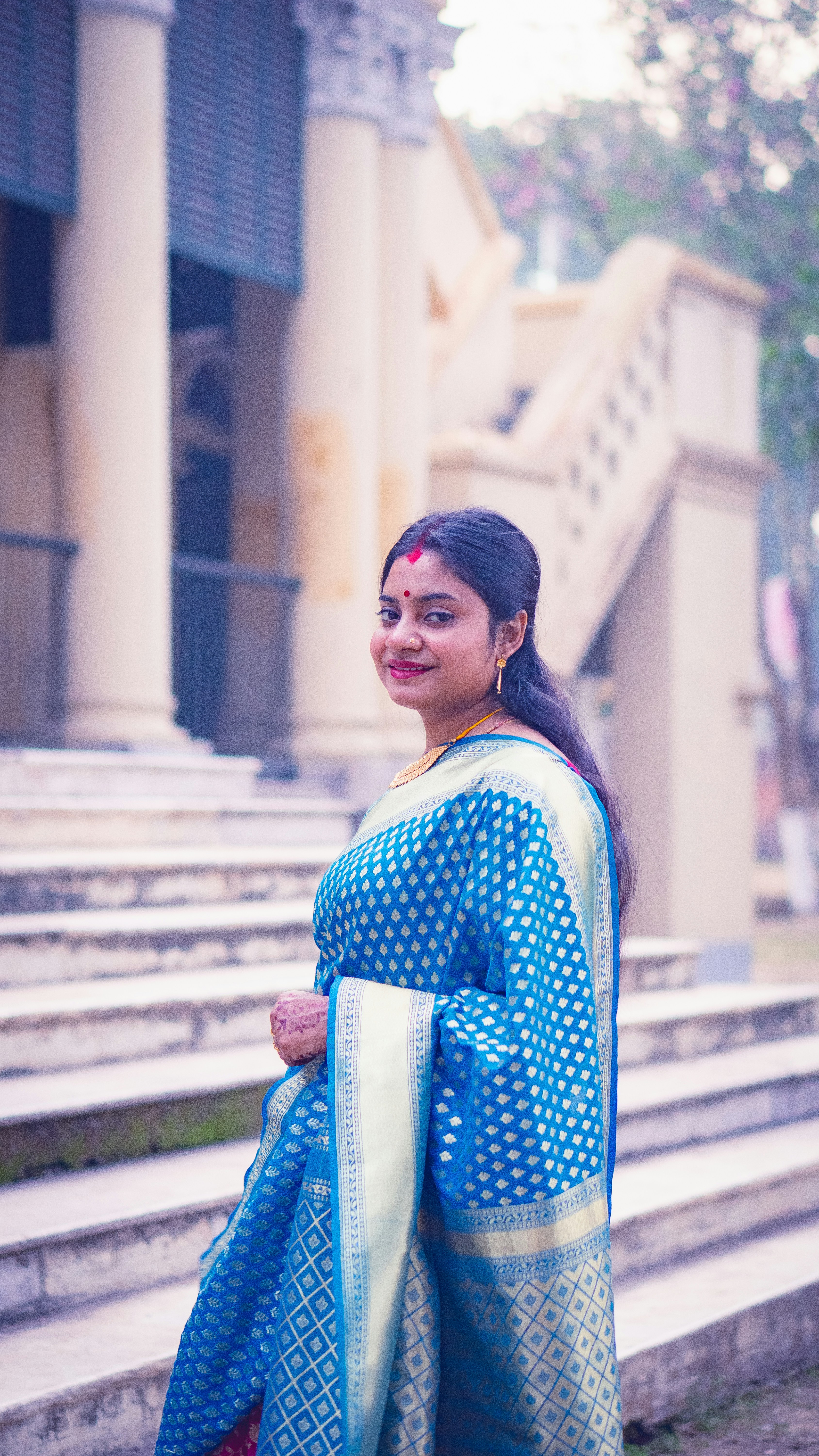 A woman in a blue patterned sari on stone steps before a building