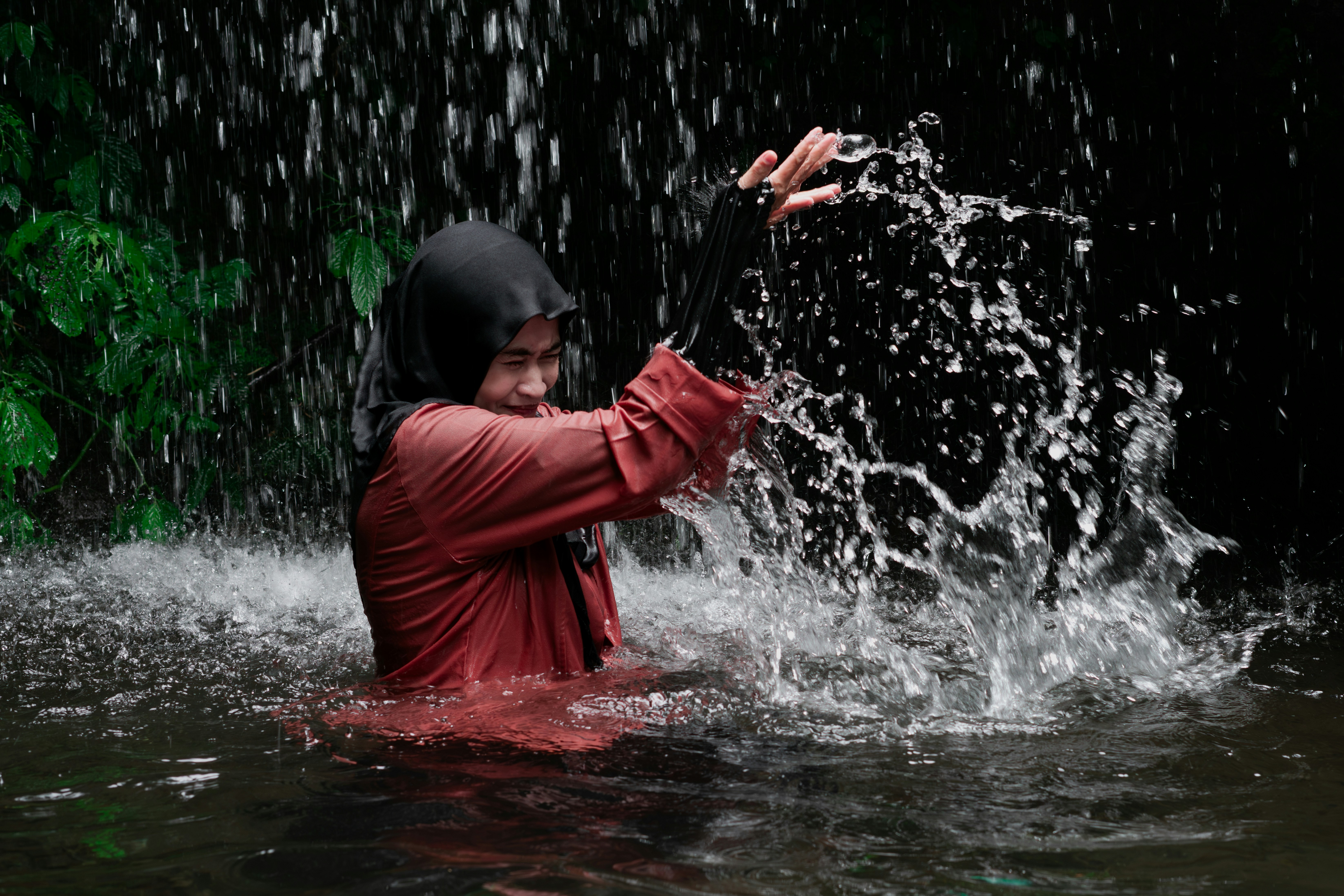 Una persona con hiyab y camiseta roja salpicando agua en una cascada