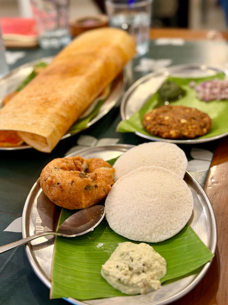 A plate with idli, vada, and chutney on a banana leaf with dosa