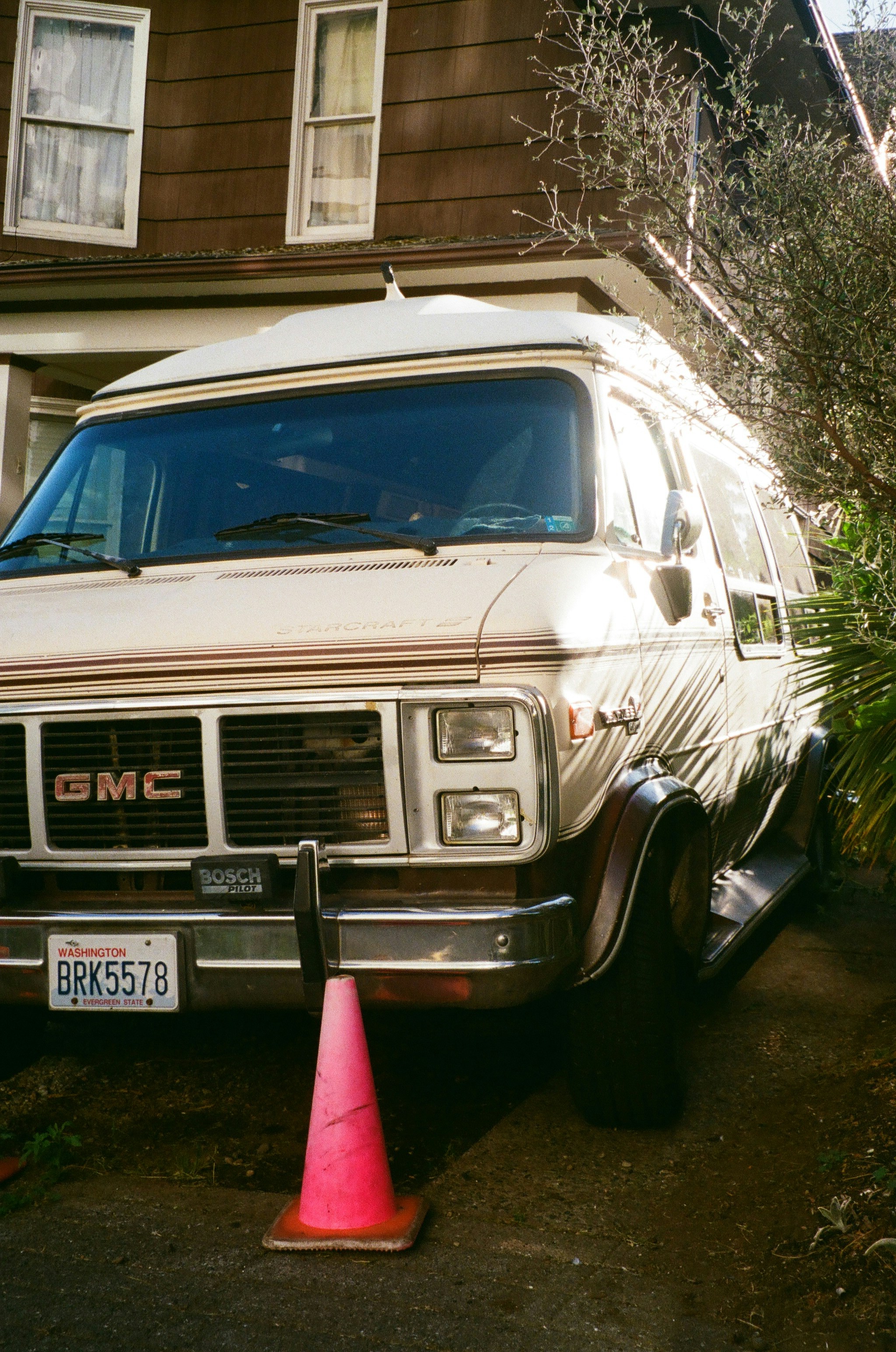 A vintage GMC van parked in a driveway with a pink traffic cone