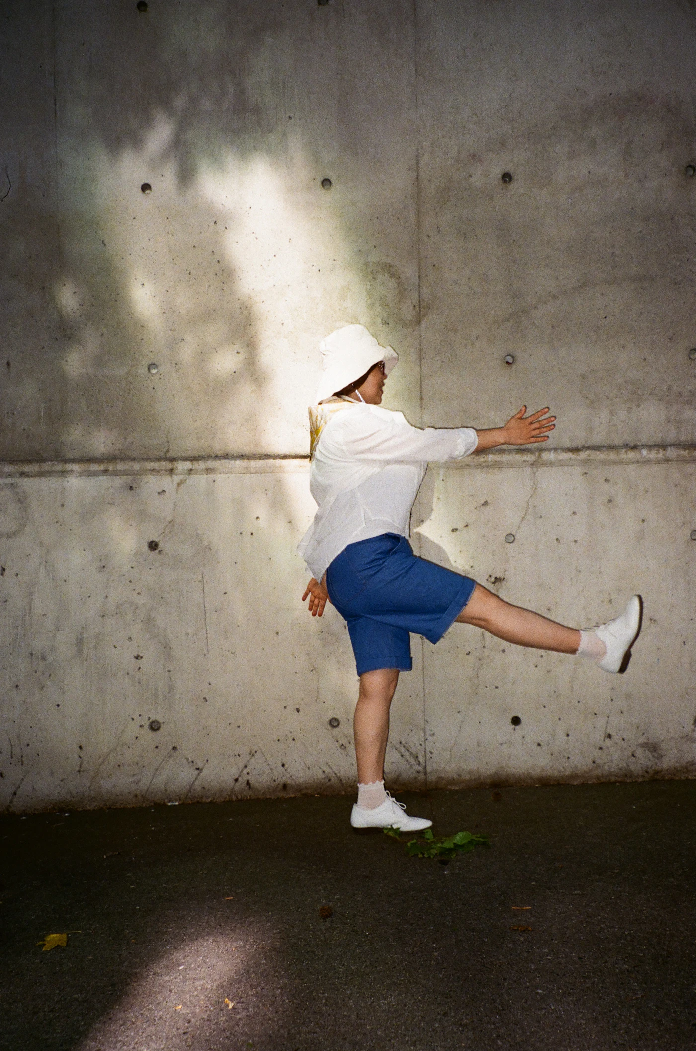 Person in white trainers kicking up a leg against a concrete wall