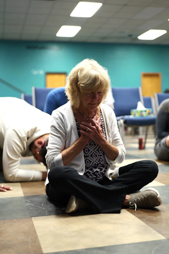An older woman sitting cross-legged on a floor with hands over her heart