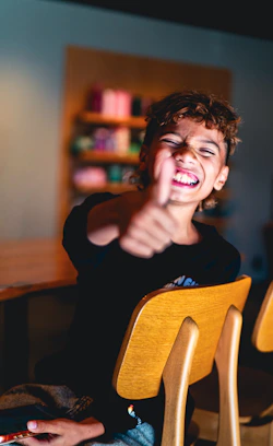 A person with curly hair giving a thumbs up in a wooden chair