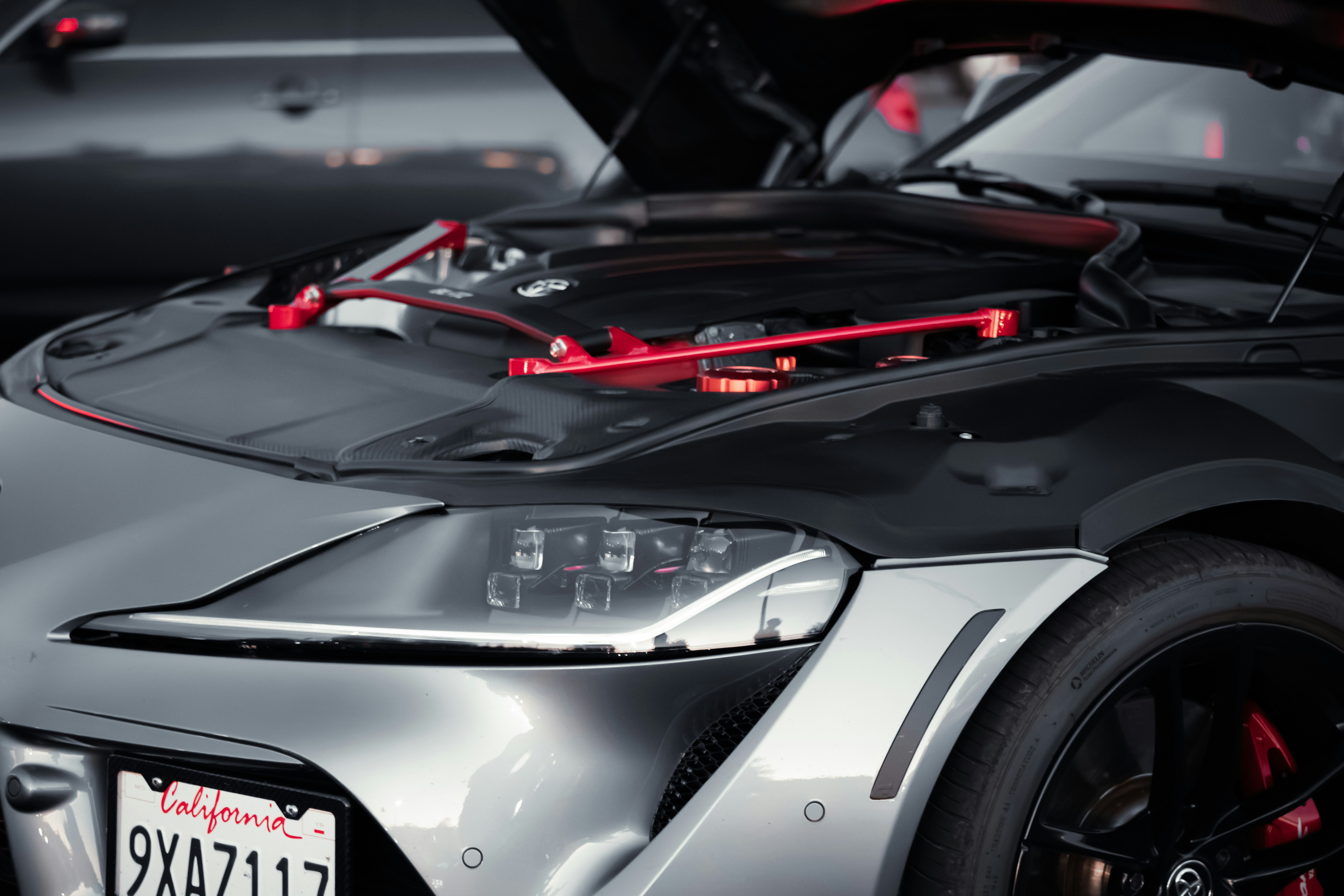A silver sports car with an open hood revealing a red engine brace