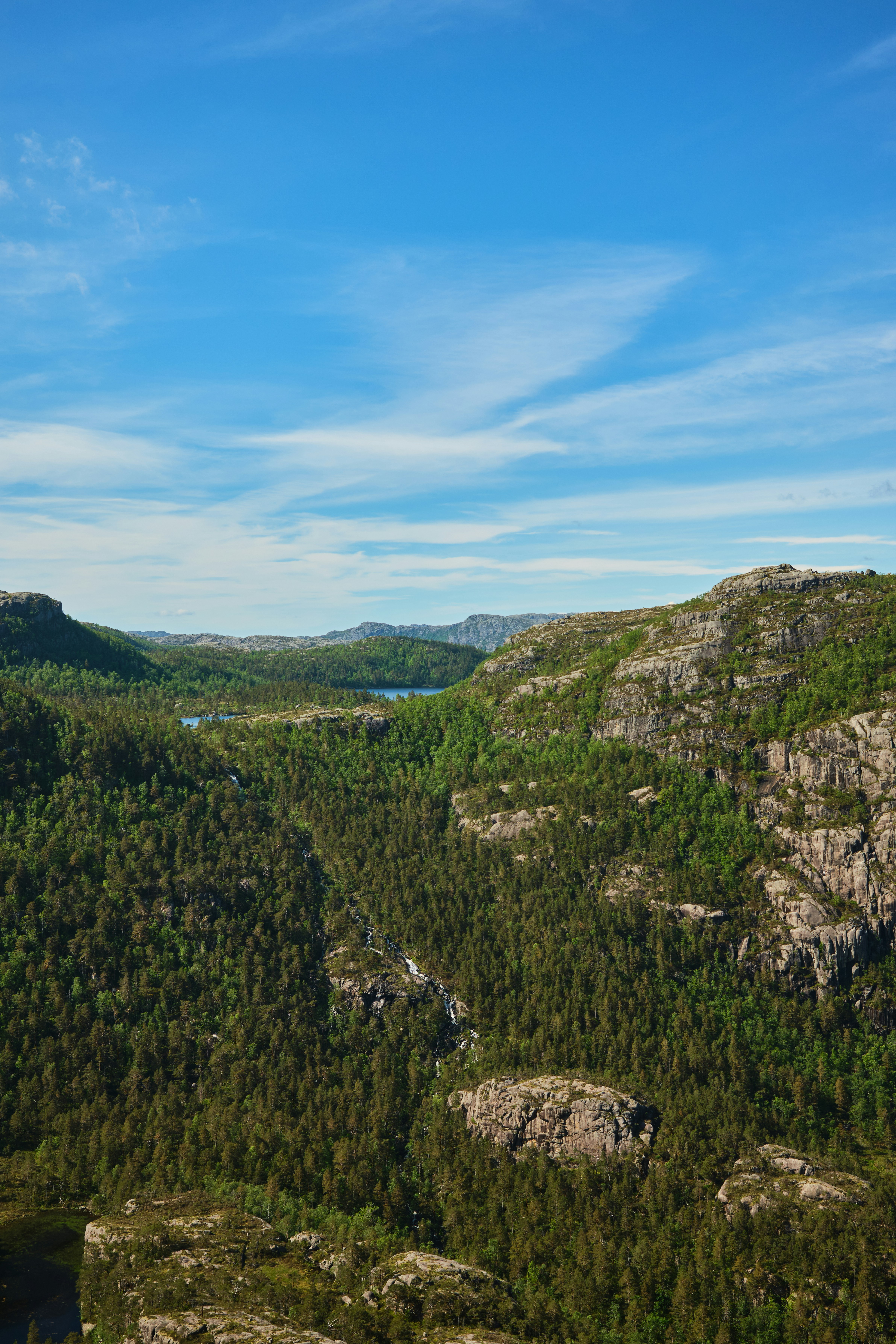 Ein schmaler Wasserfall, der unter blauem Himmel einen bewaldeten Berghang hinabstürzt