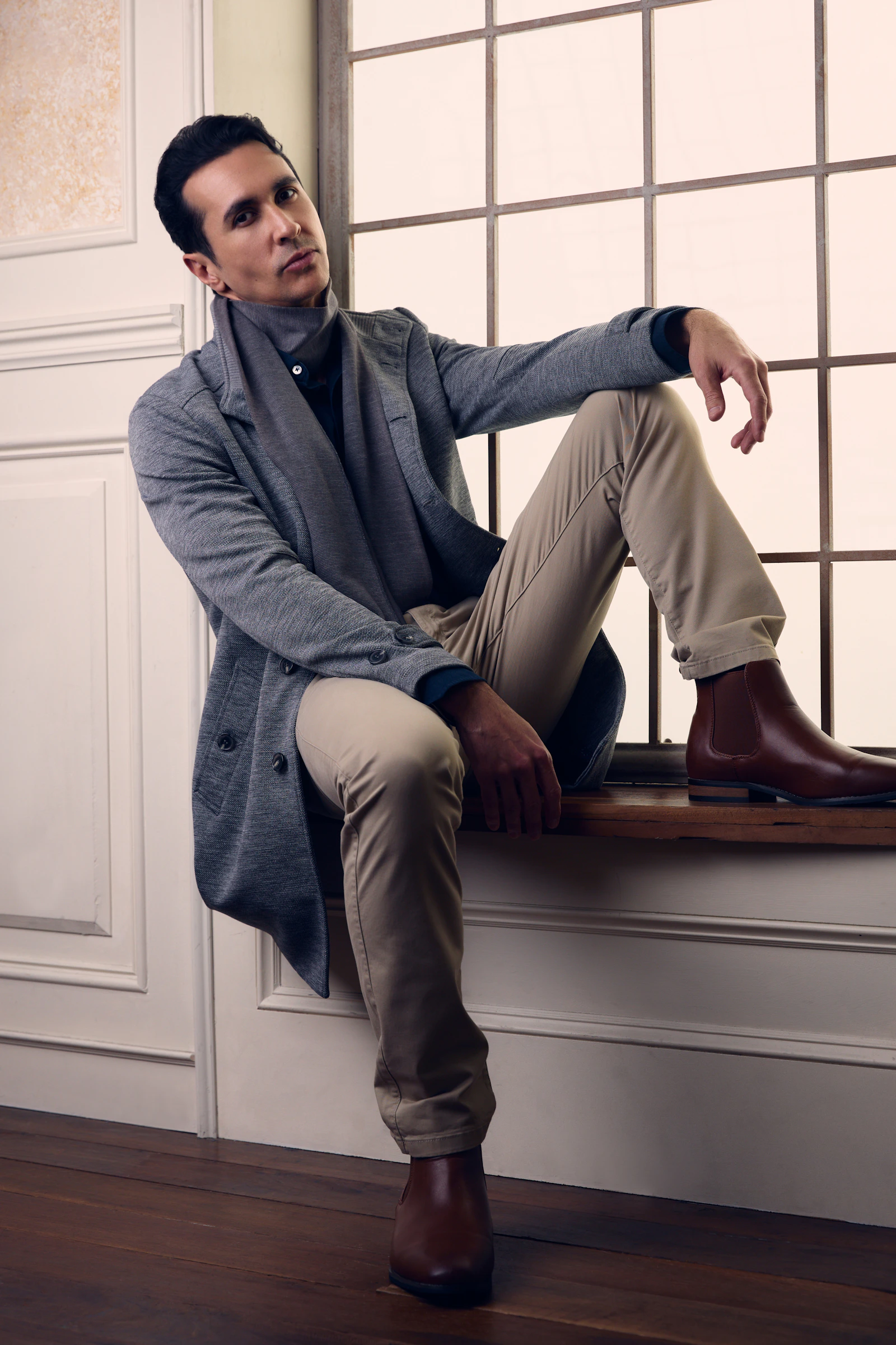 Man in grey coat and beige trousers by window