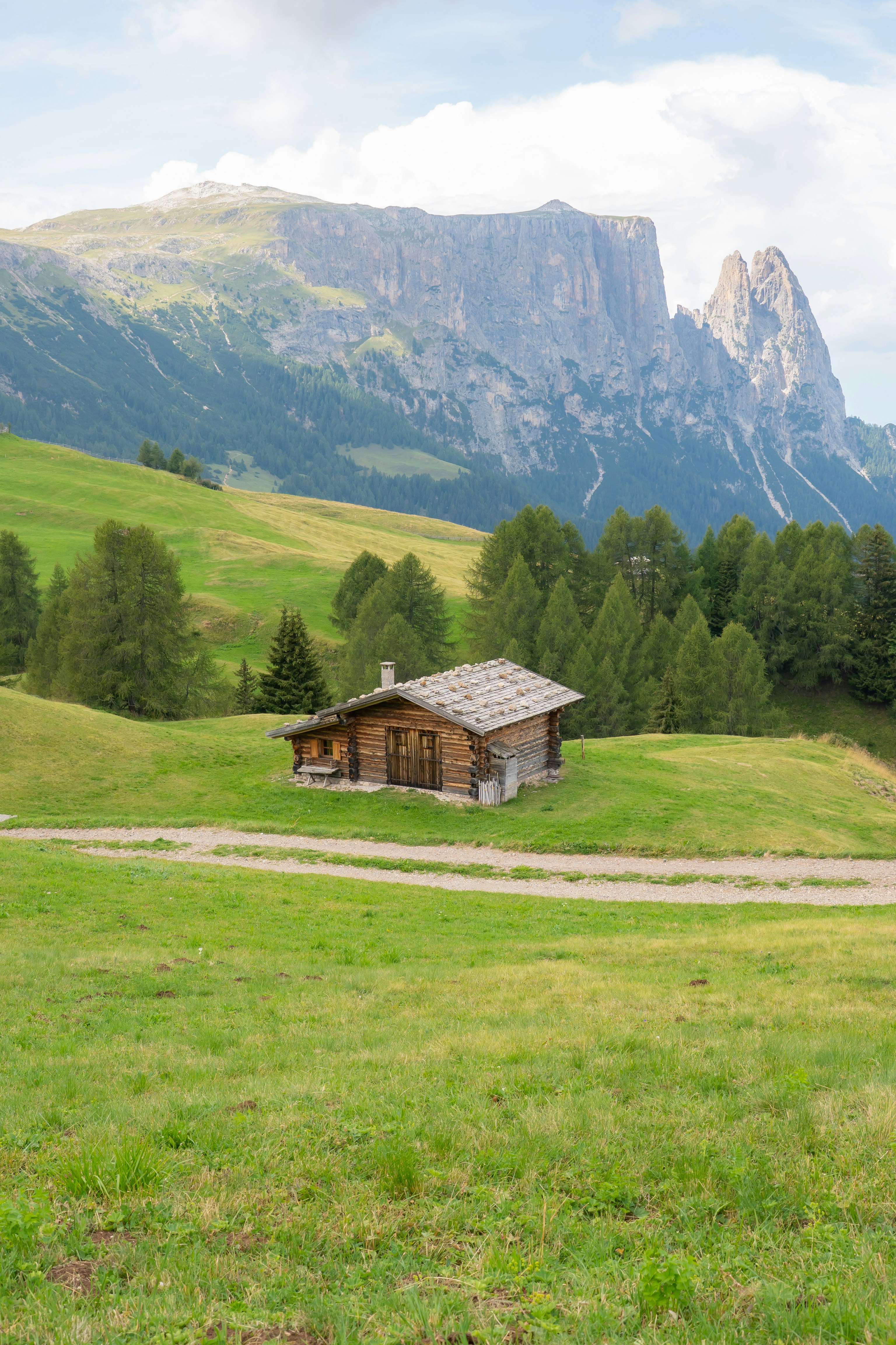 Eine Holzhütte auf einer grünen Alpenwiese unterhalb eines felsigen Gebirges