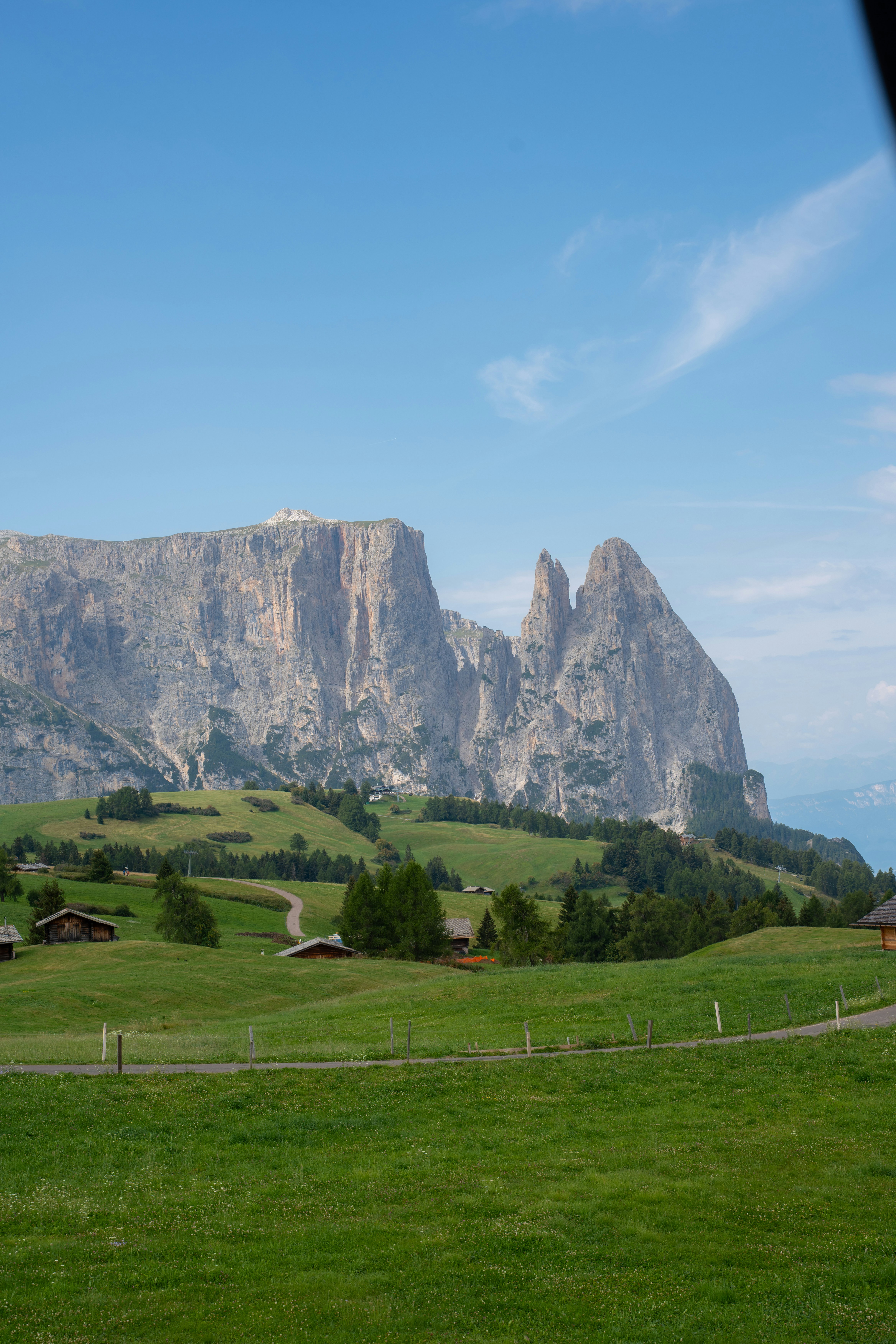 Eine grüne Bergweide mit kleinen Holzhütten unterhalb des zerklüfteten Schlern-Massivs