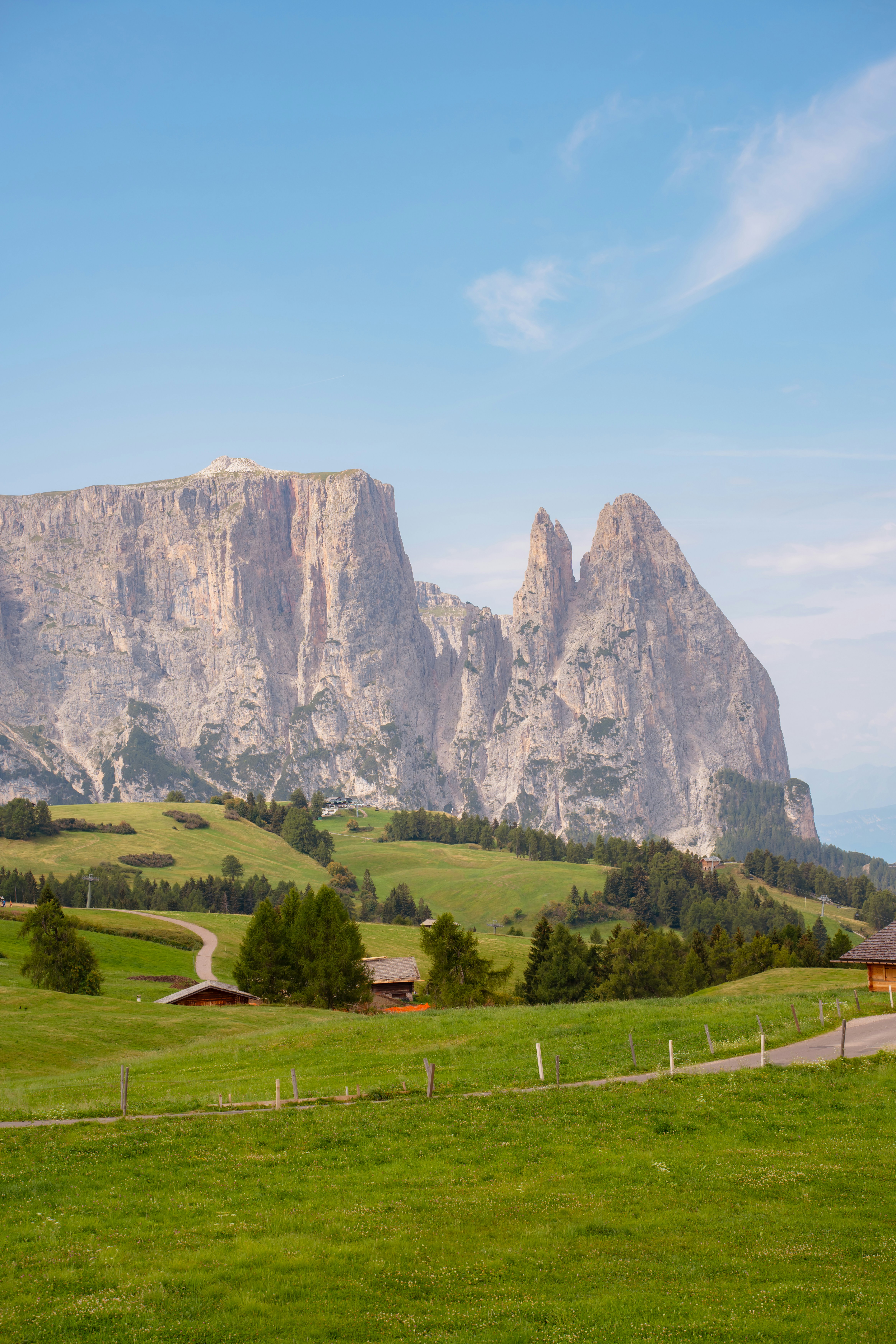 Eine grüne Wiese mit Holzhütten unterhalb der zerklüfteten Gipfel der Dolomiten