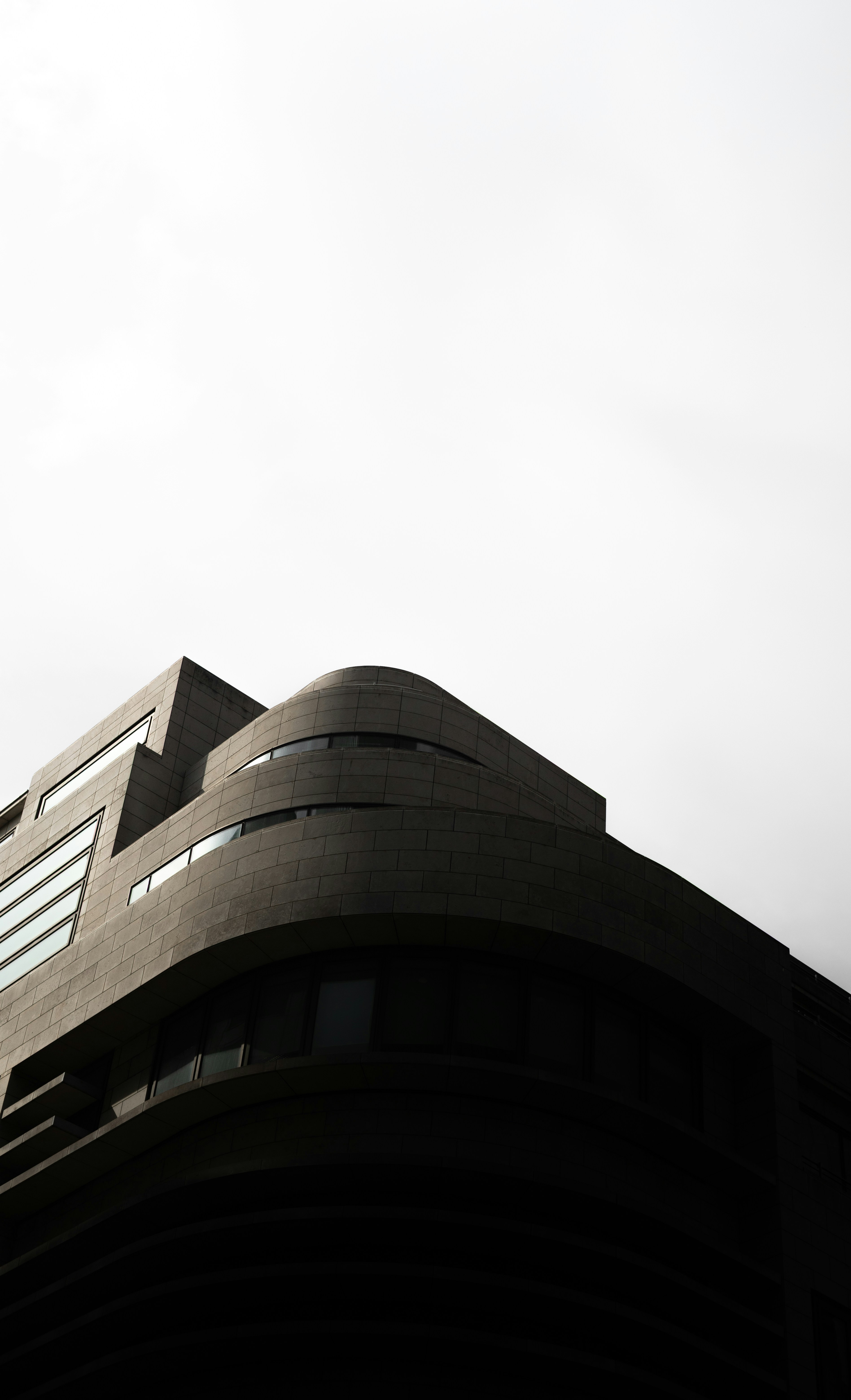 Una esquina curva de un edificio moderno de piedra gris contra un cielo brillante