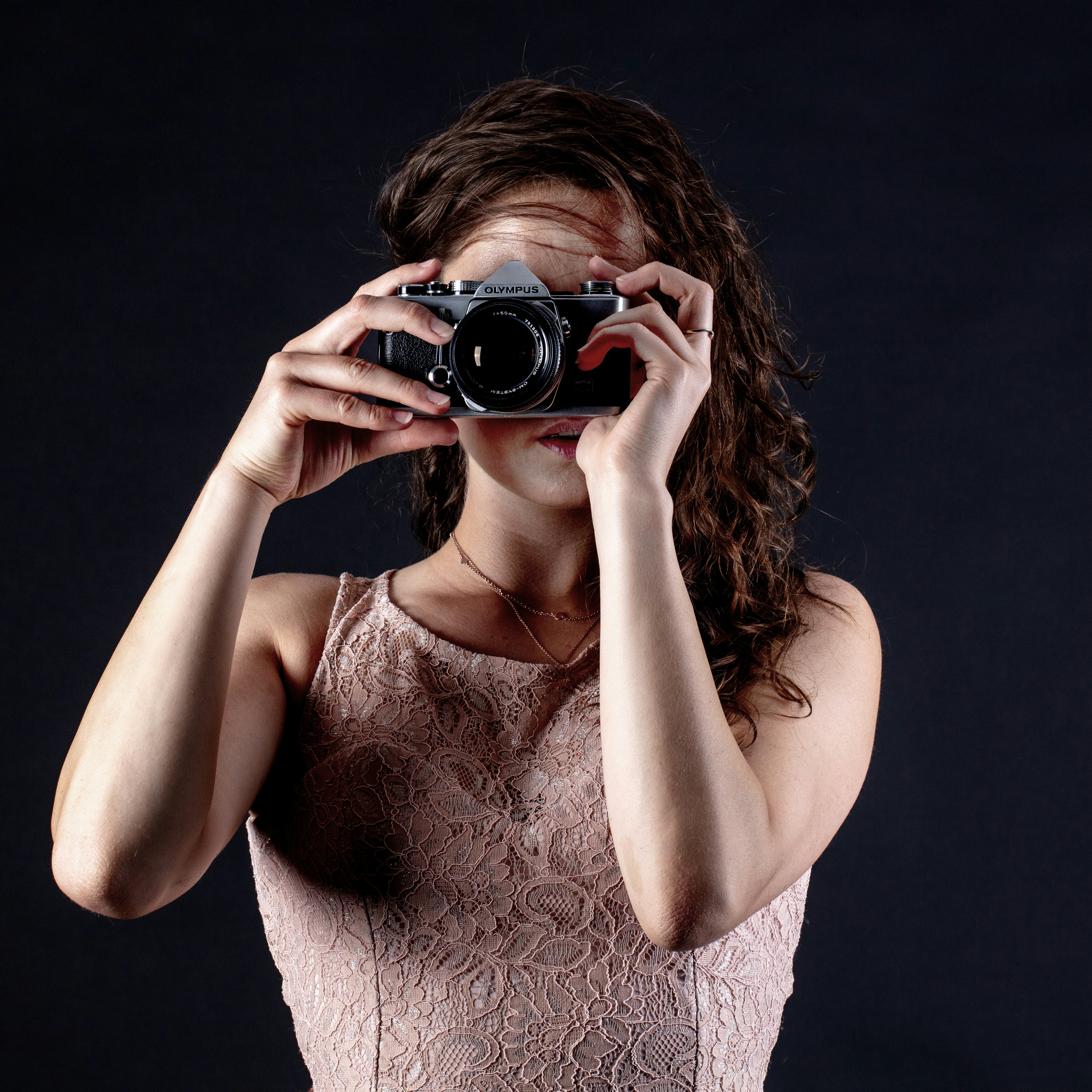 A woman in a lace top holding an Olympus camera to her face