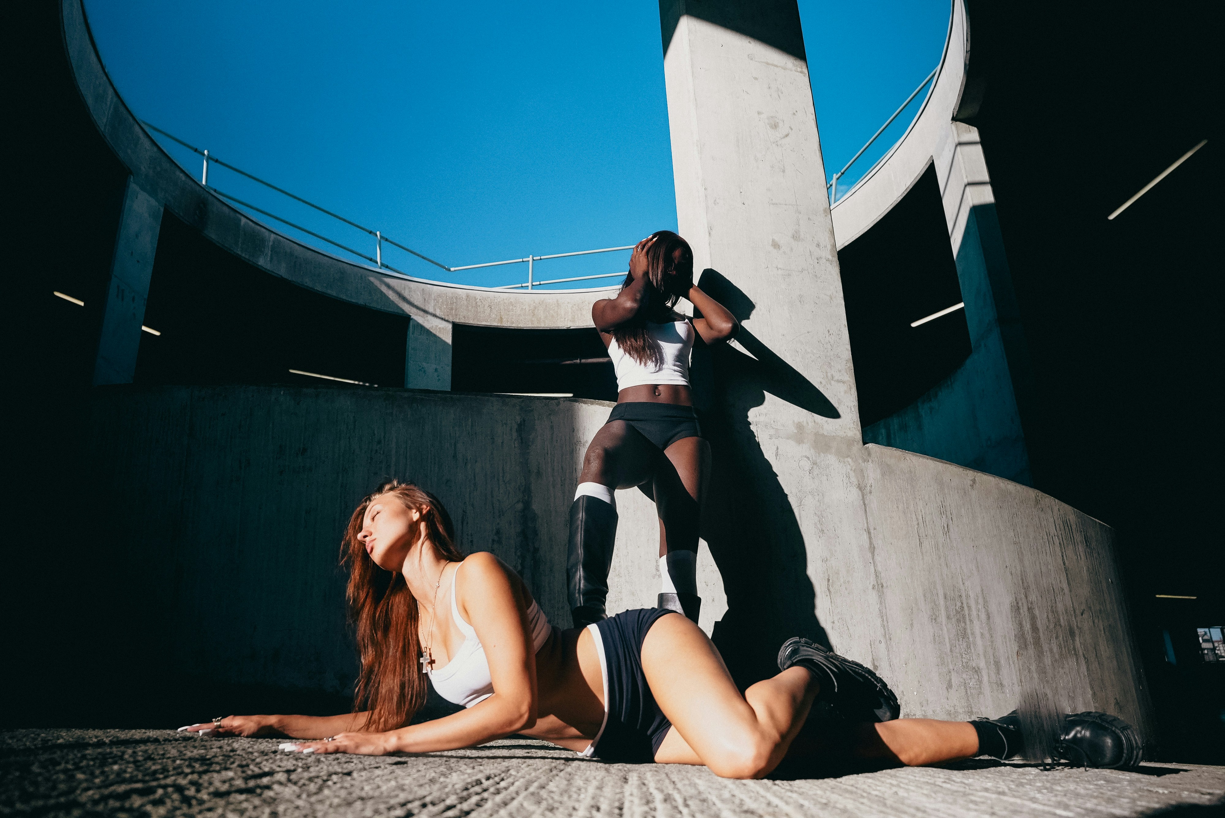 Two women in white crop tops and black shorts posing in a concrete parking structure