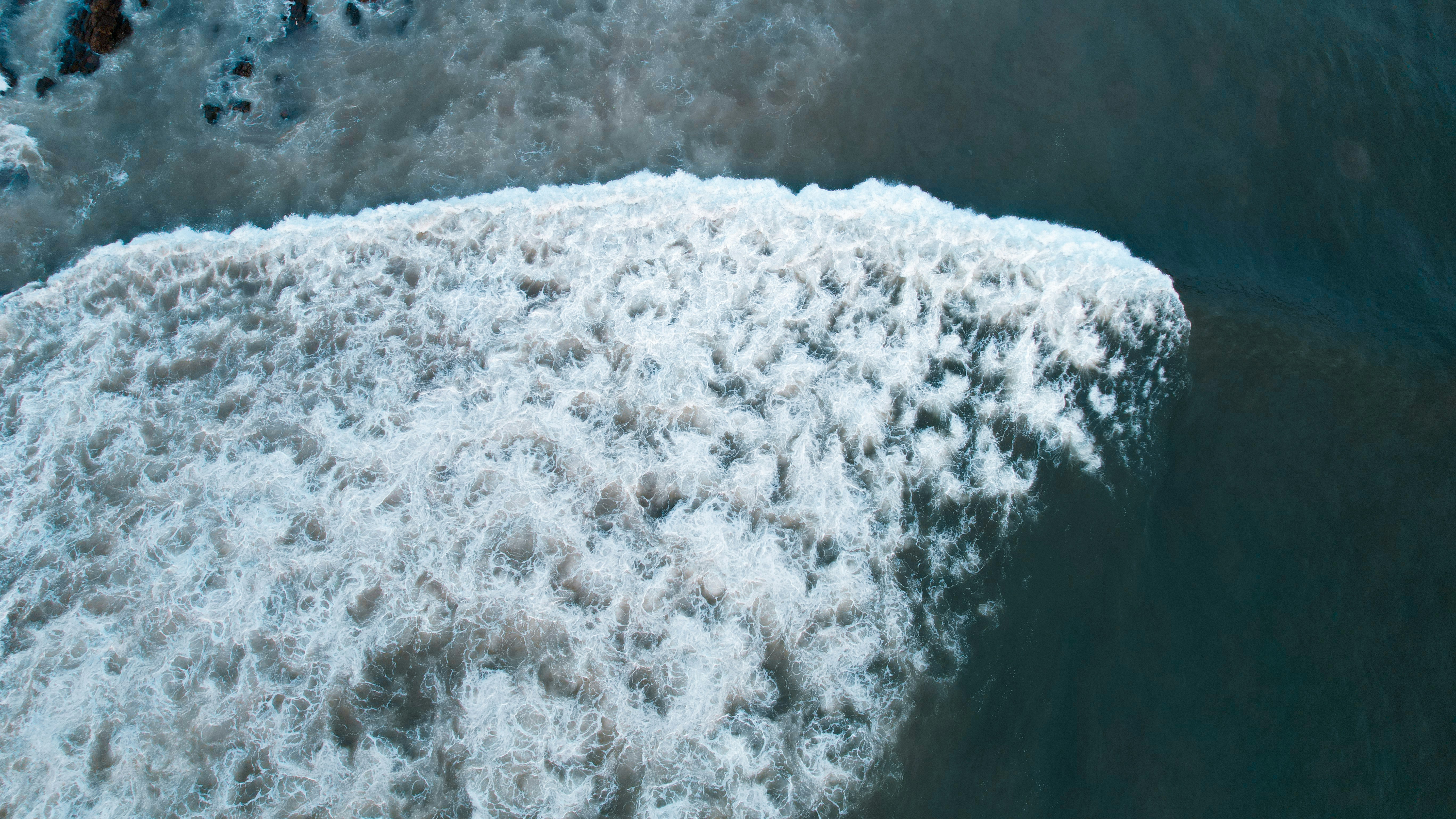 An aerial view of a white breaking wave on dark blue ocean water