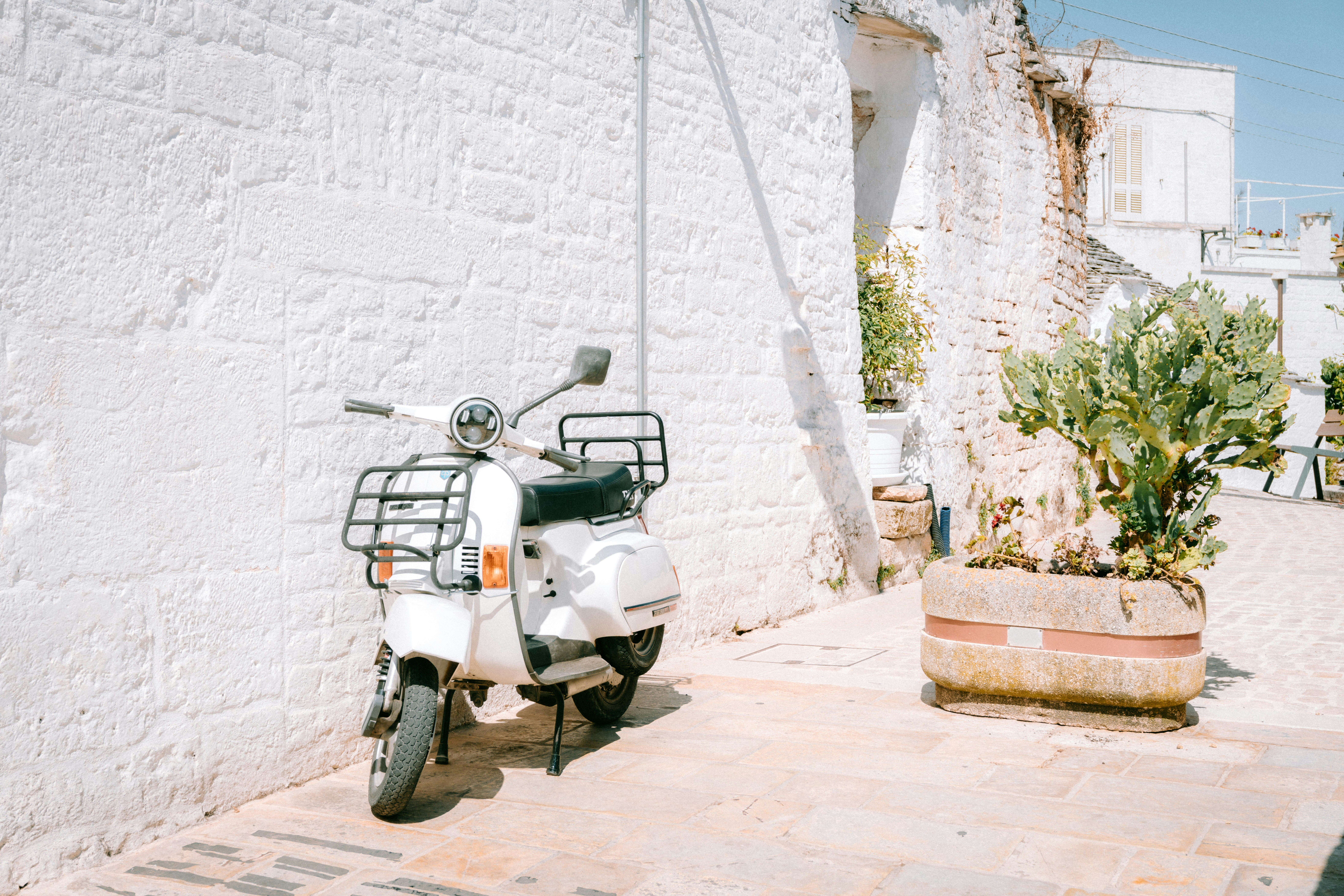 A white moped parked by a sunlit white wall next to a planter