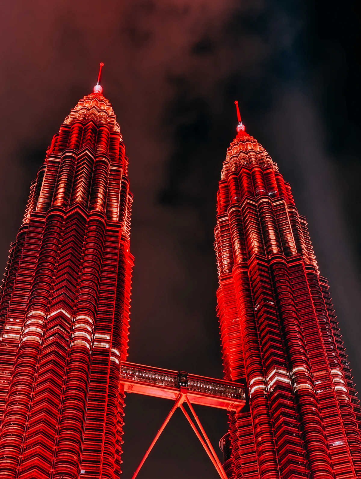 Petronas Twin Towers illuminated in red at night, seen from below with the skybridge between them
