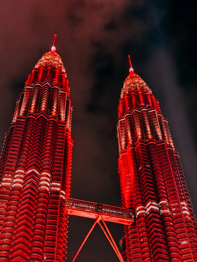 Petronas Twin Towers illuminated in red at night, seen from below with the skybridge between them