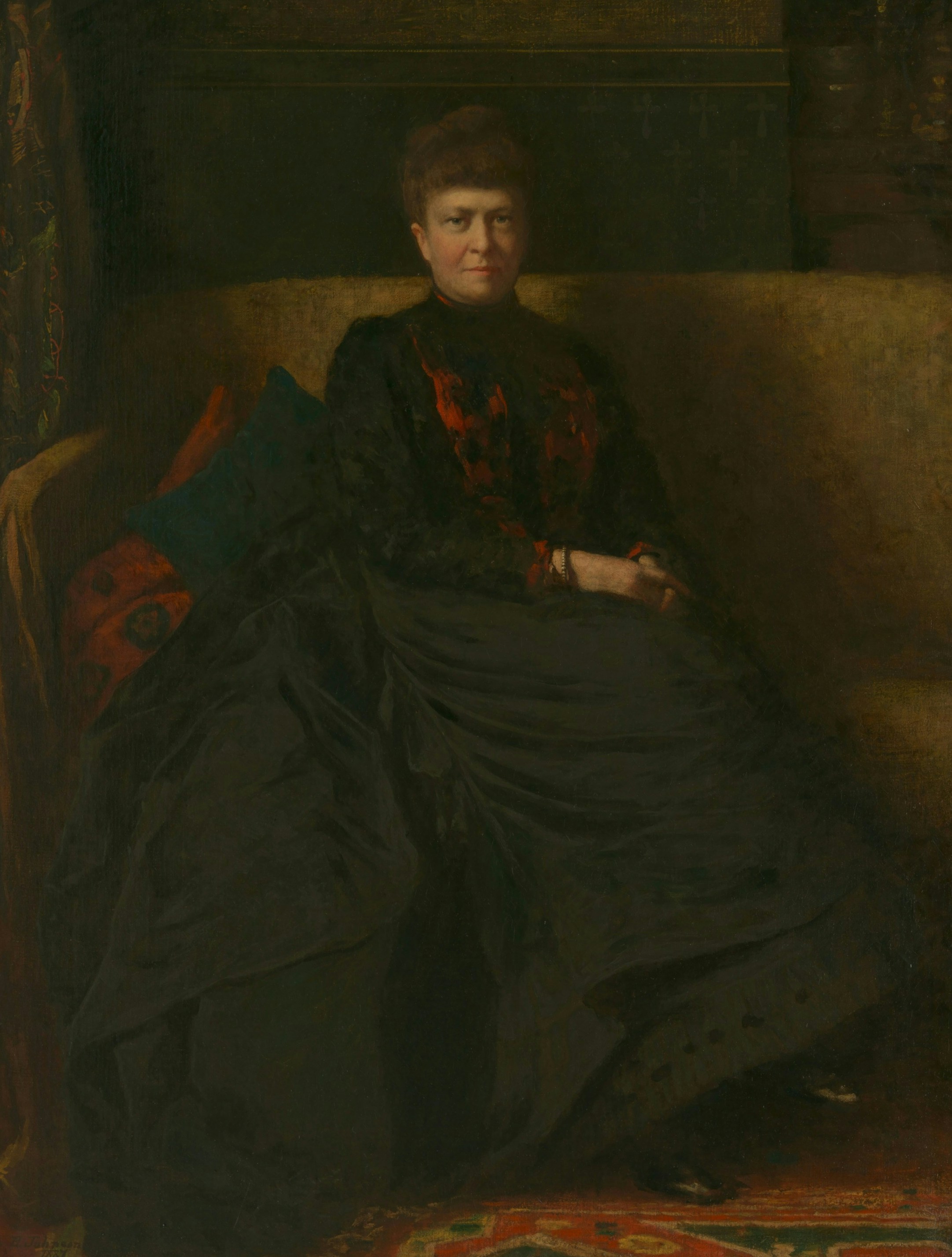 Eine Frau in einem dunklen Kleid mit roten Akzenten sitzt auf einem Sofa
