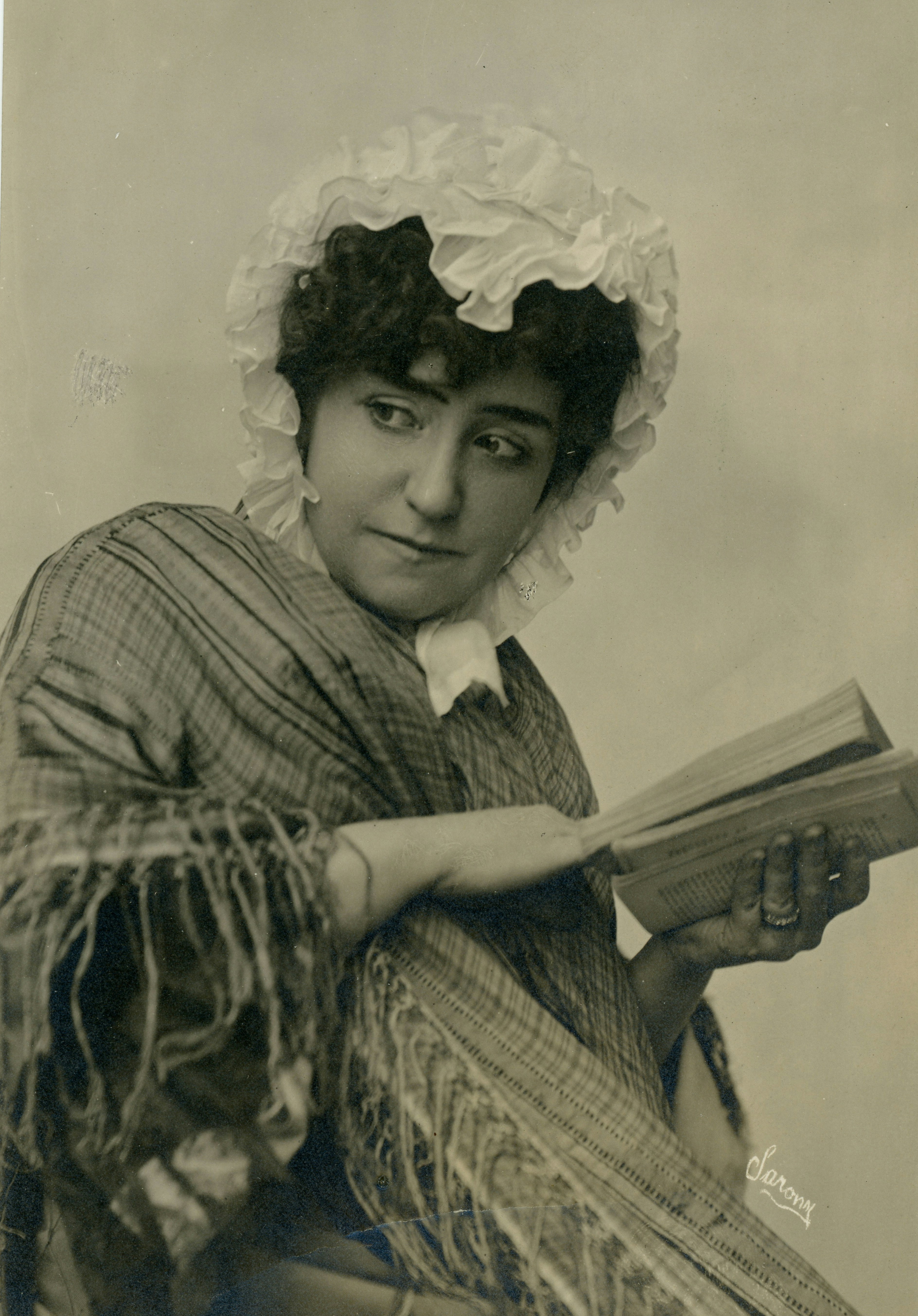 Eine Frau mit Rüschenhaube und kariertem Schal, die ein Buch liest