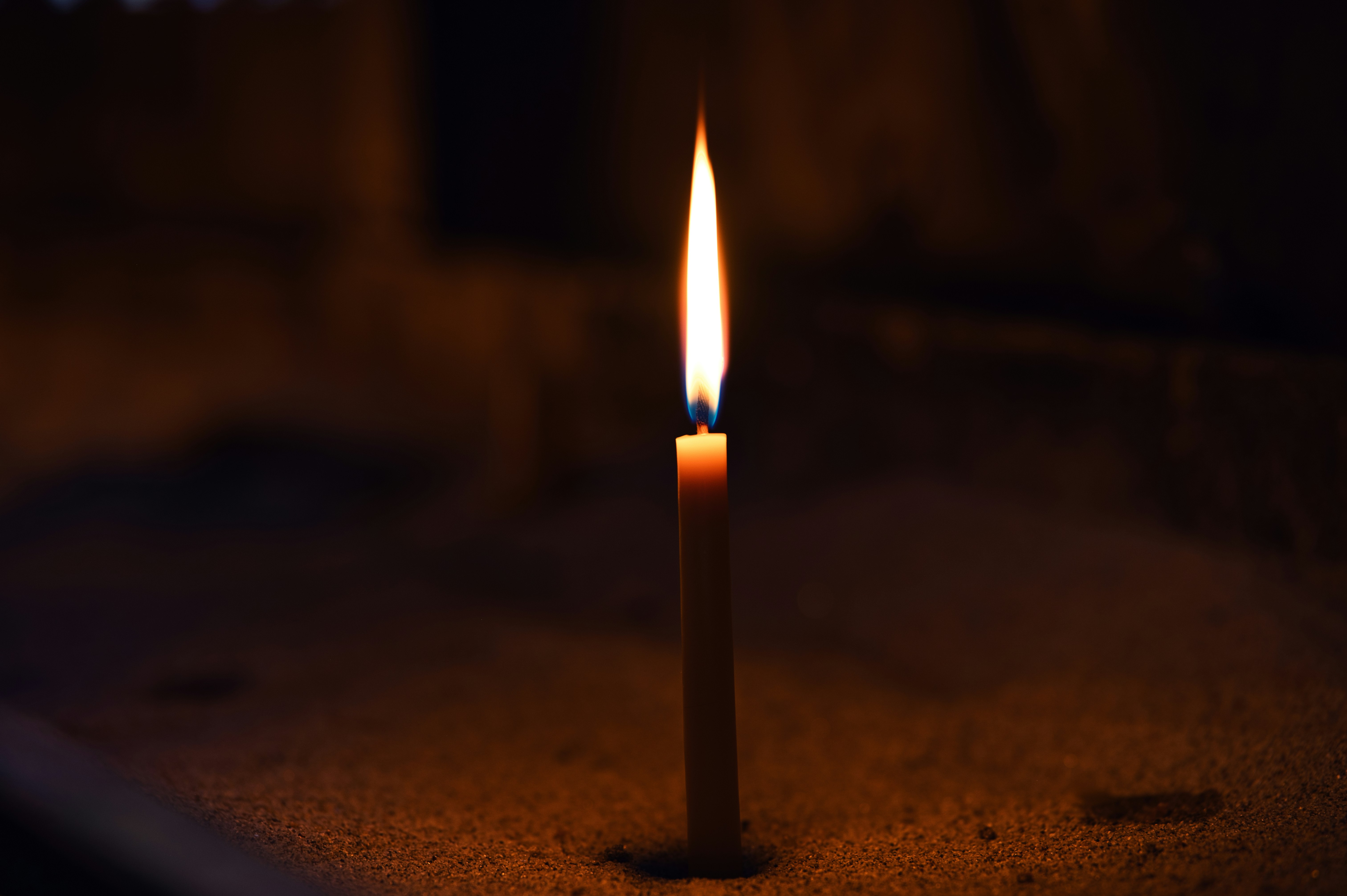 A single lit candle with a bright flame in a dark room