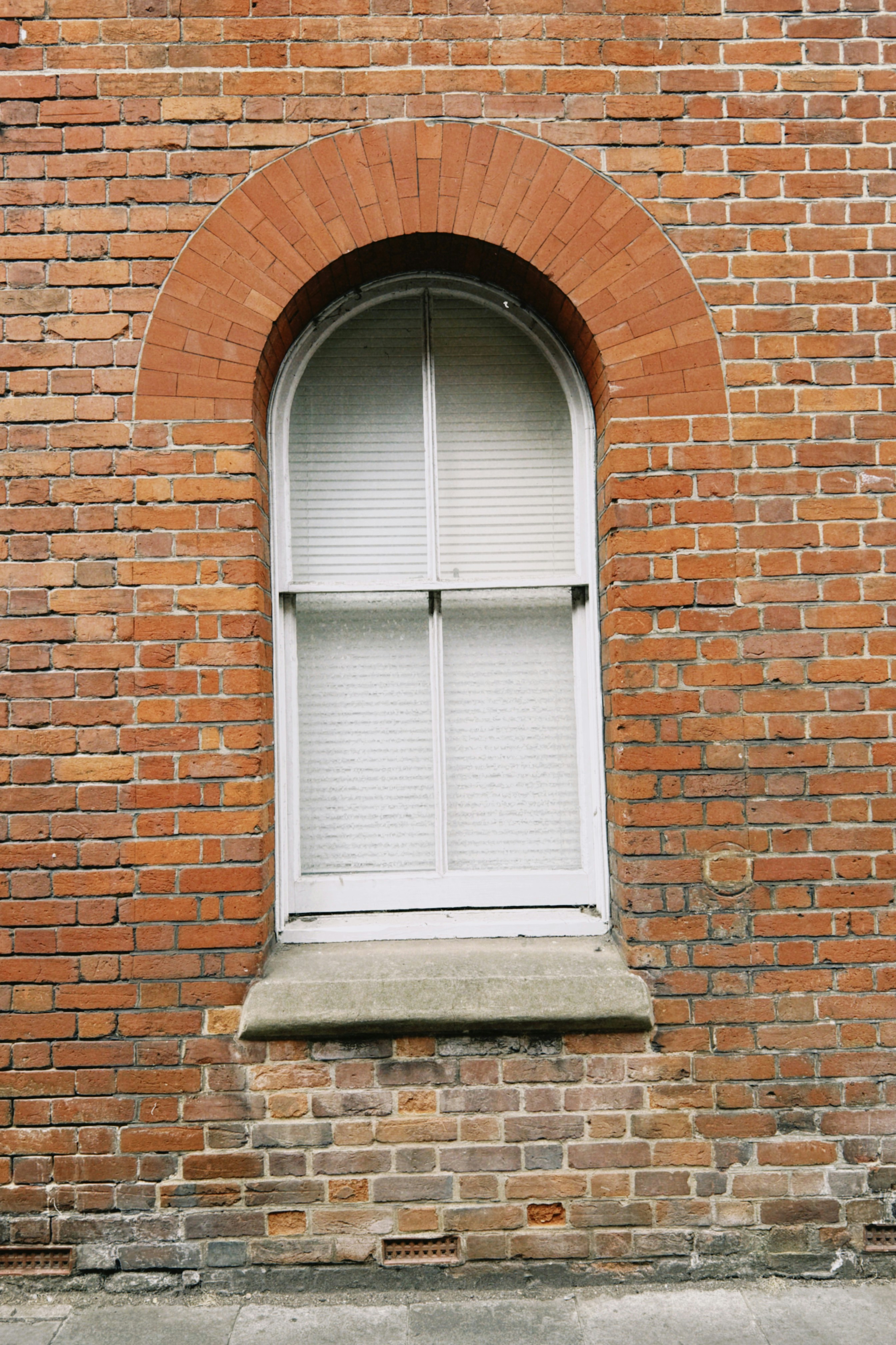 An arched window with white blinds set into a red brick wall