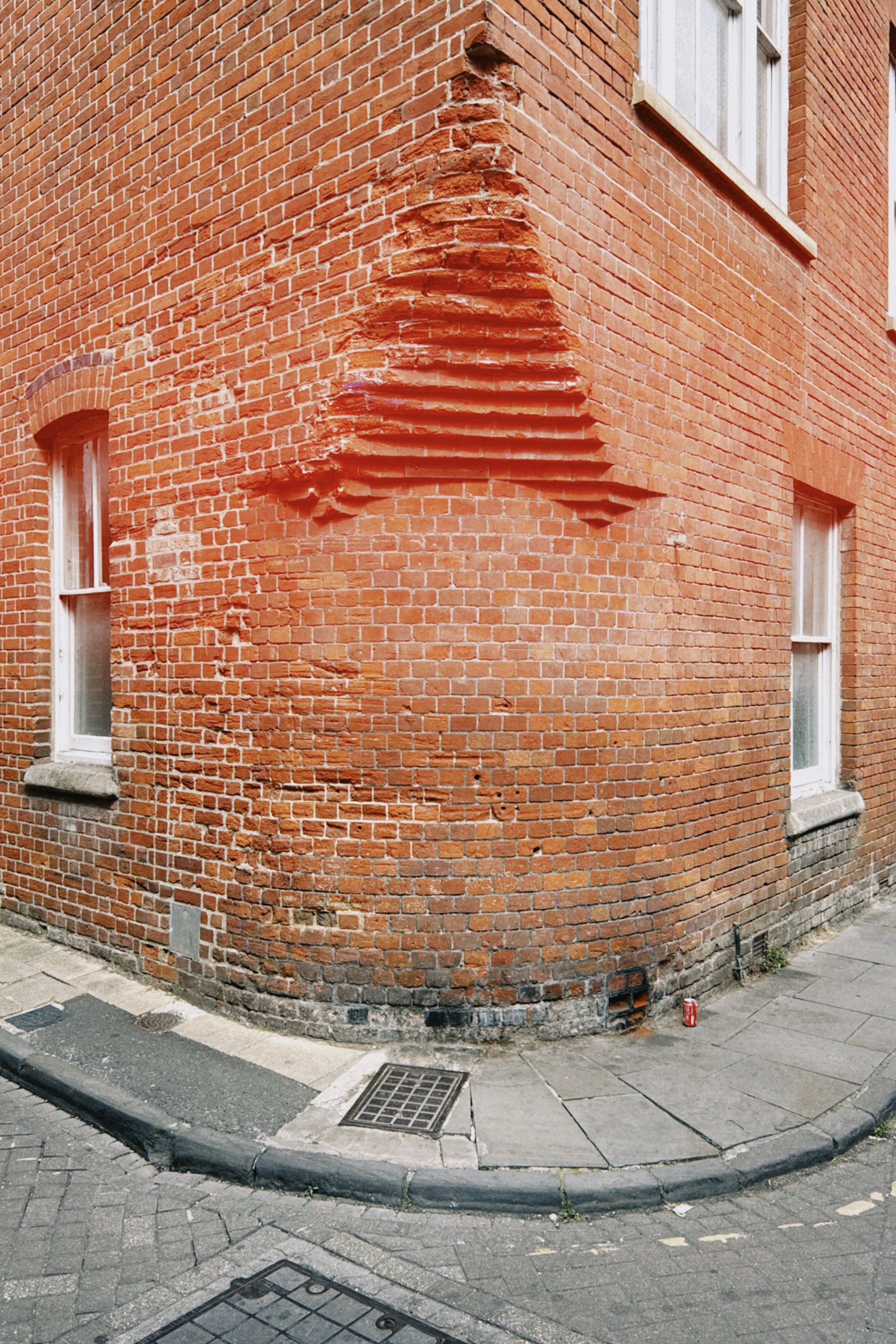 A weathered red brick building corner with damaged masonry above a city sidewalk