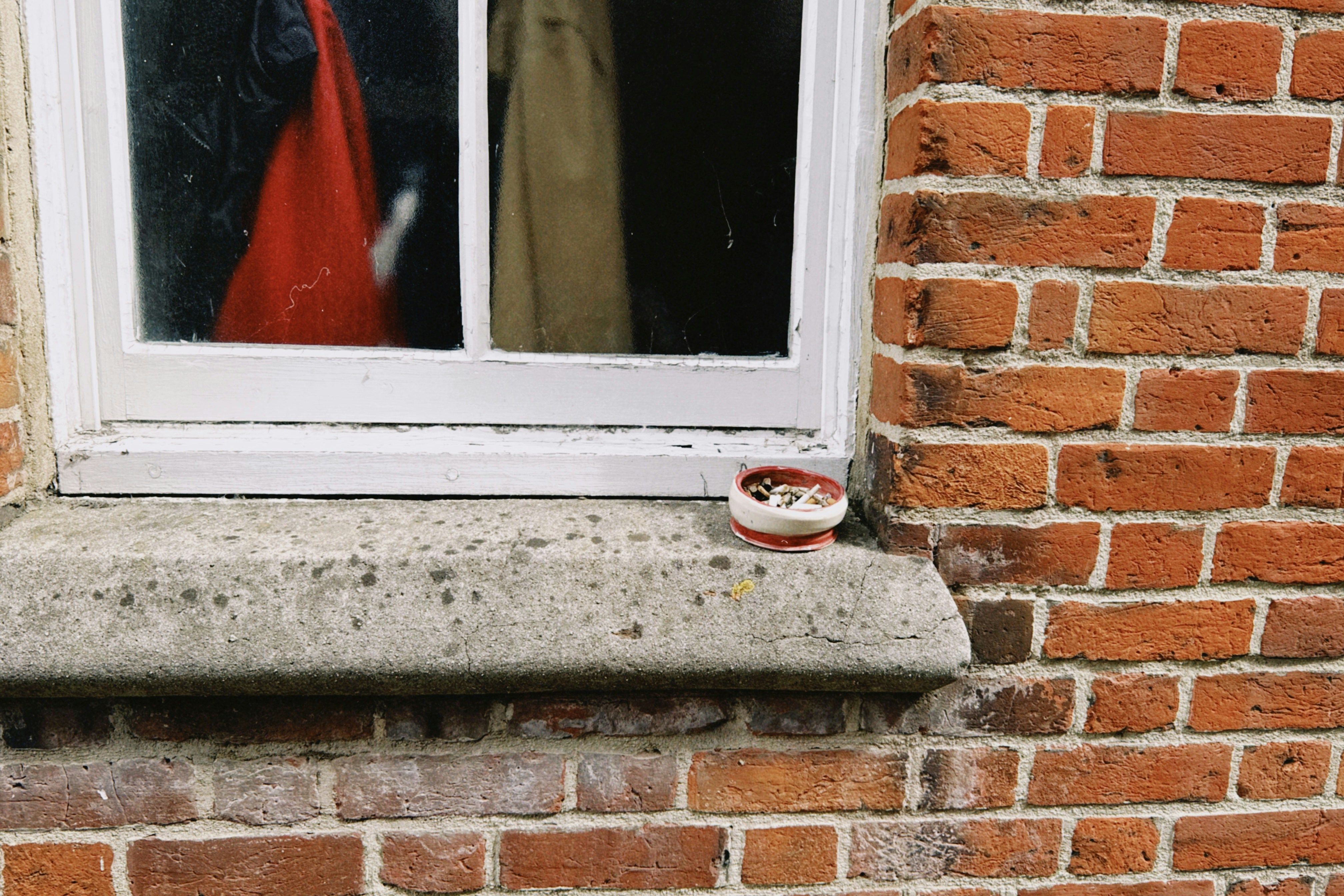 A small ceramic ashtray with cigarette butts on a stone windowsill by a window