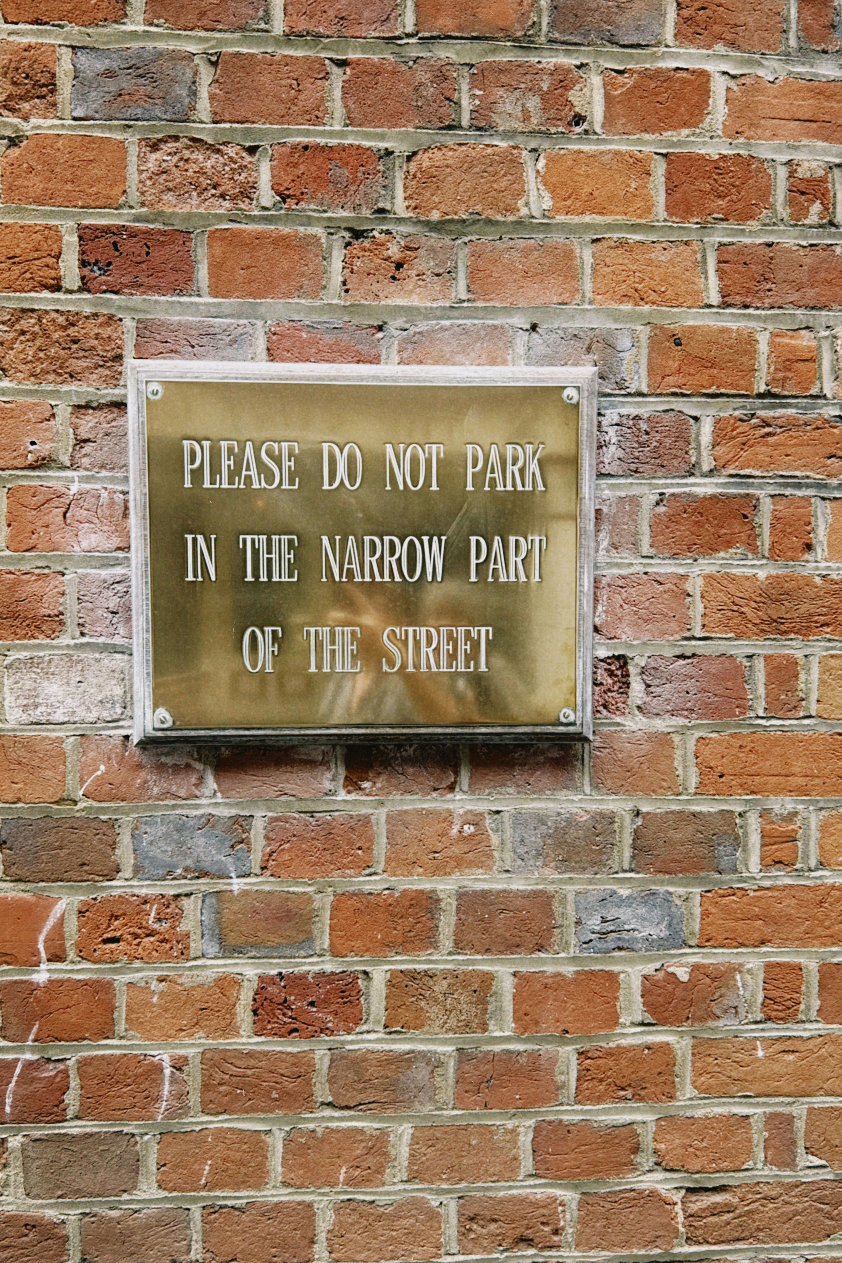 A brass sign on a brick wall reading "PLEASE DO NOT PARK"