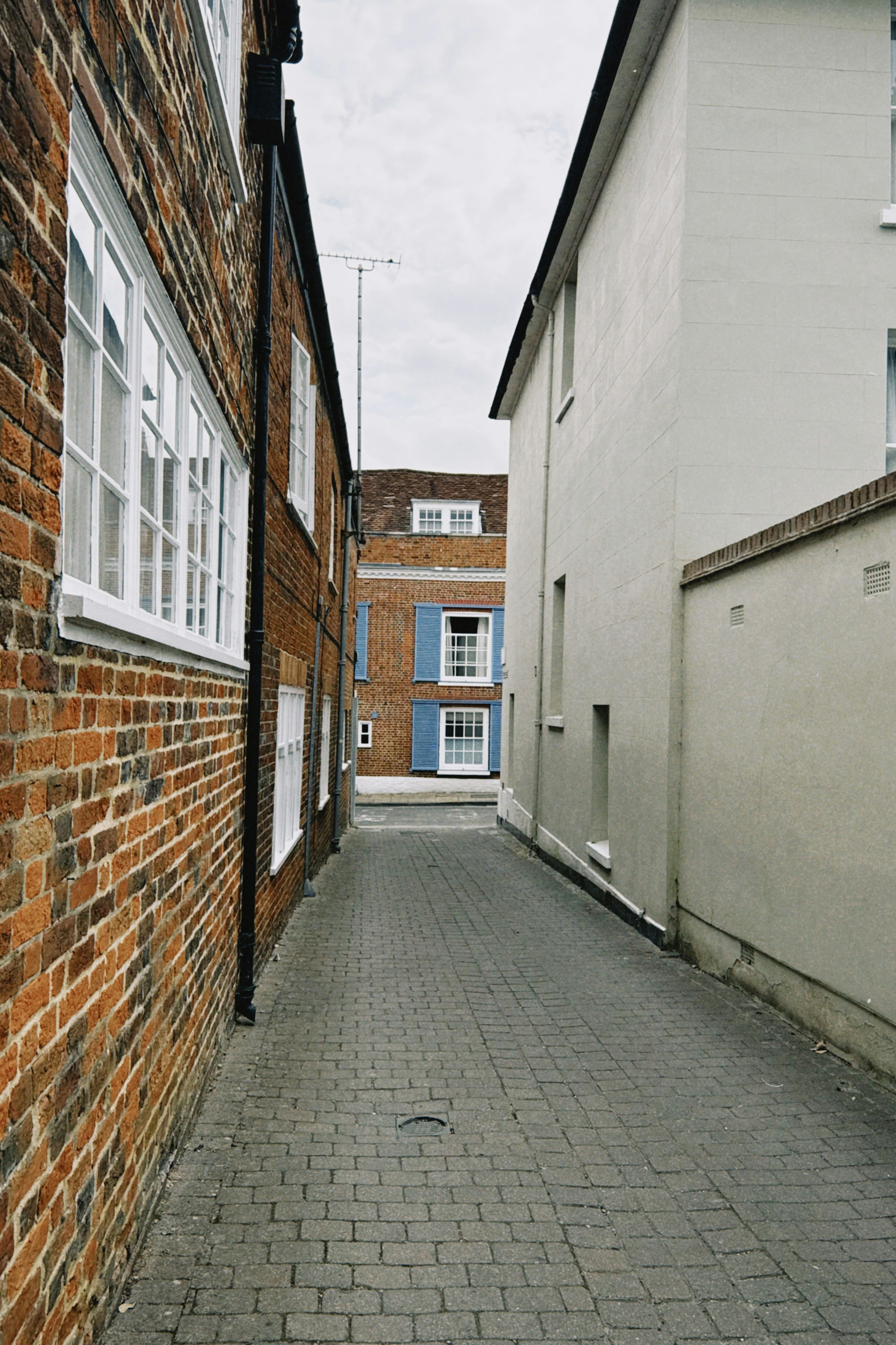 A narrow cobblestone alleyway between a brick building and a smooth white wall