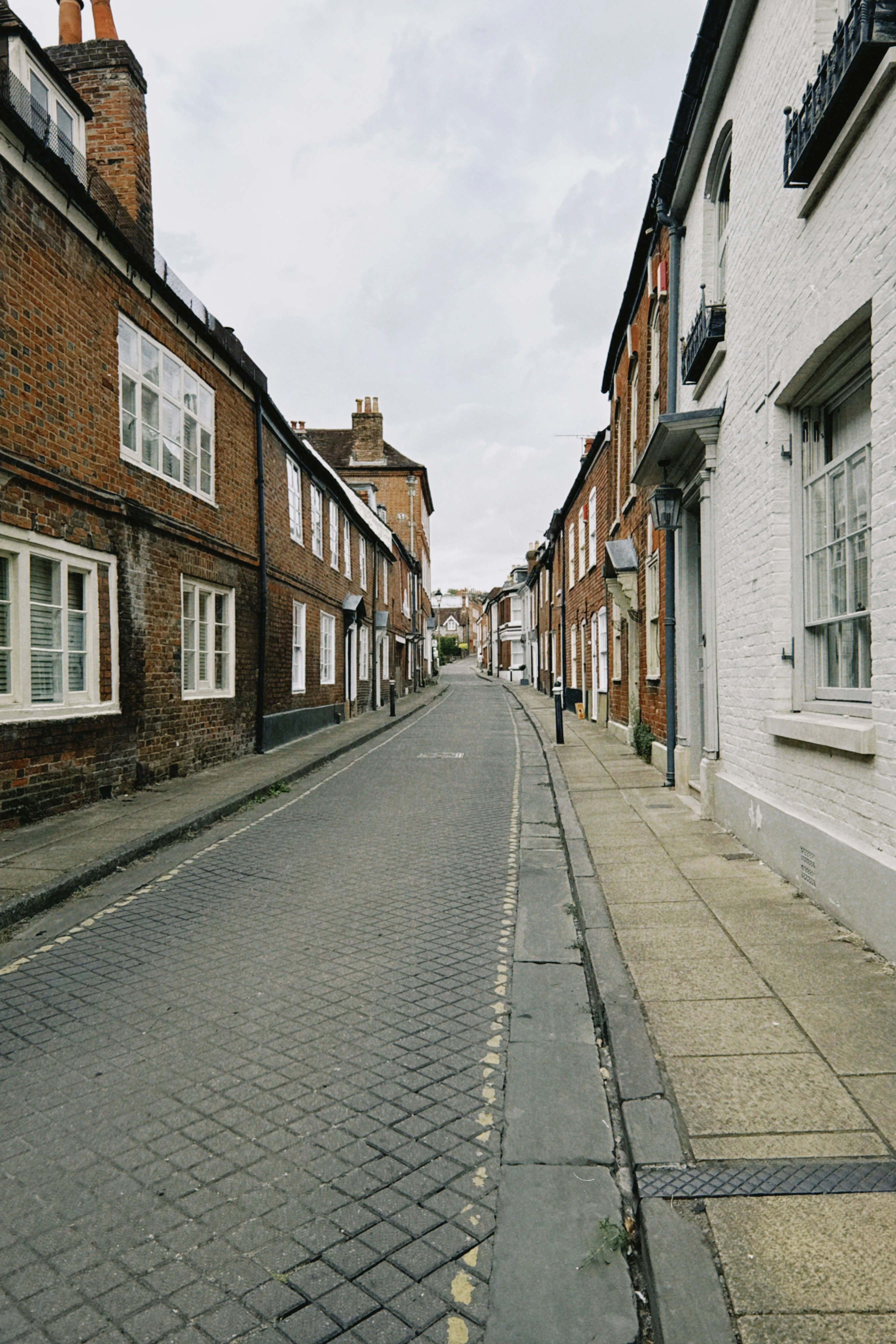 A narrow cobblestone street lined with historic brick buildings under a cloudy sky