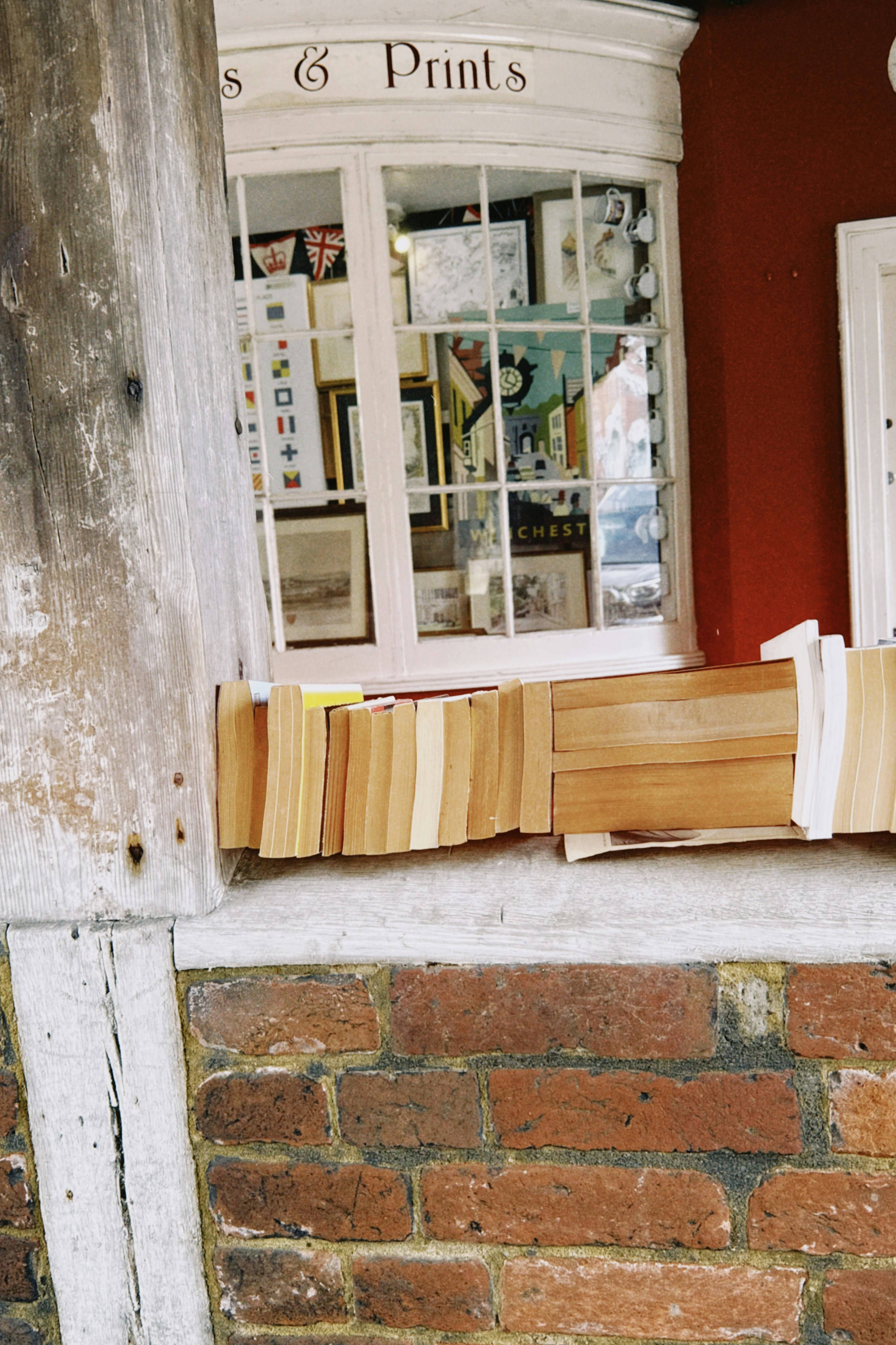 A row of books on a brick ledge in front of a shop window