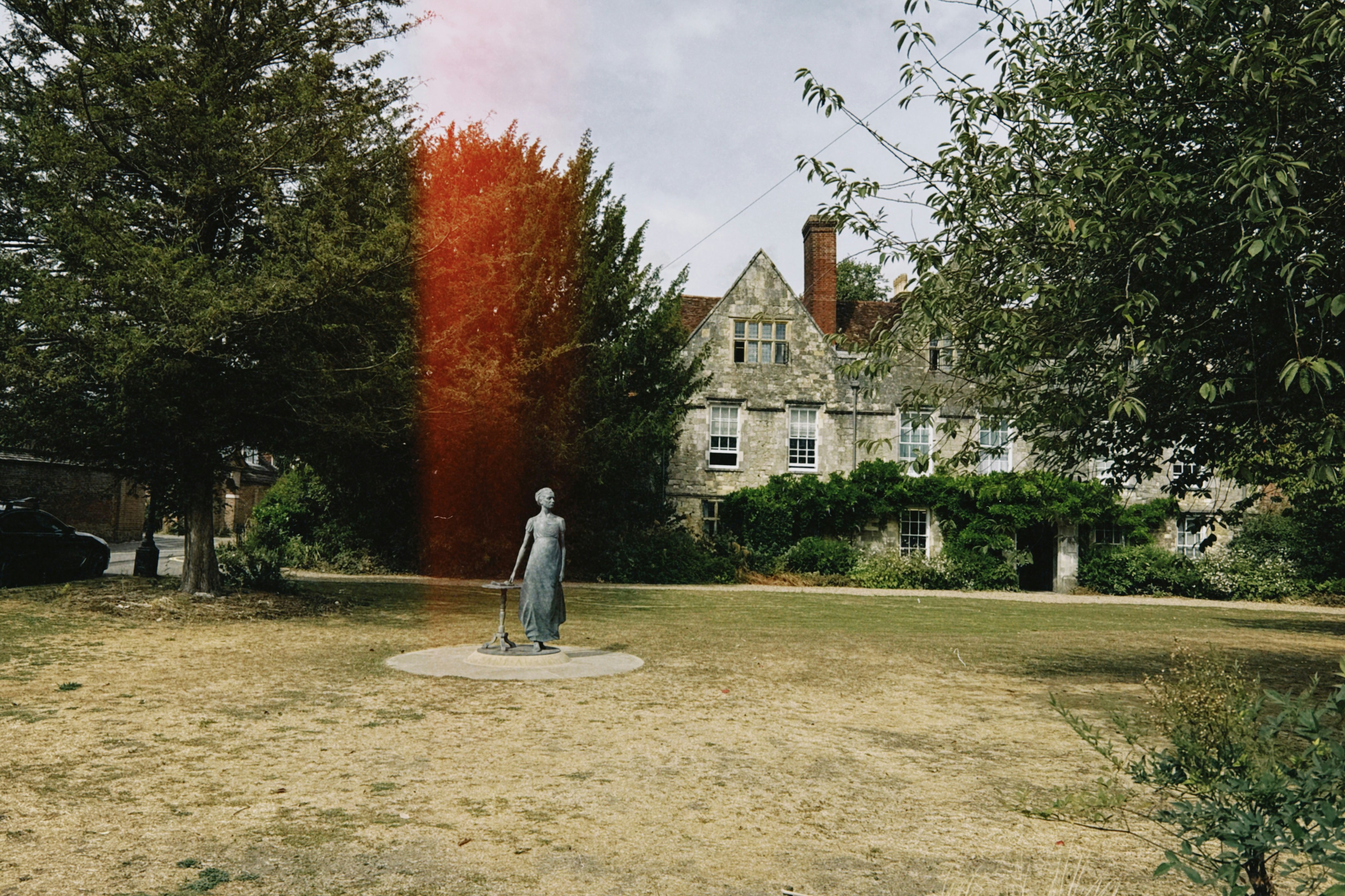 A bronze statue of a woman on a lawn before a stone manor house