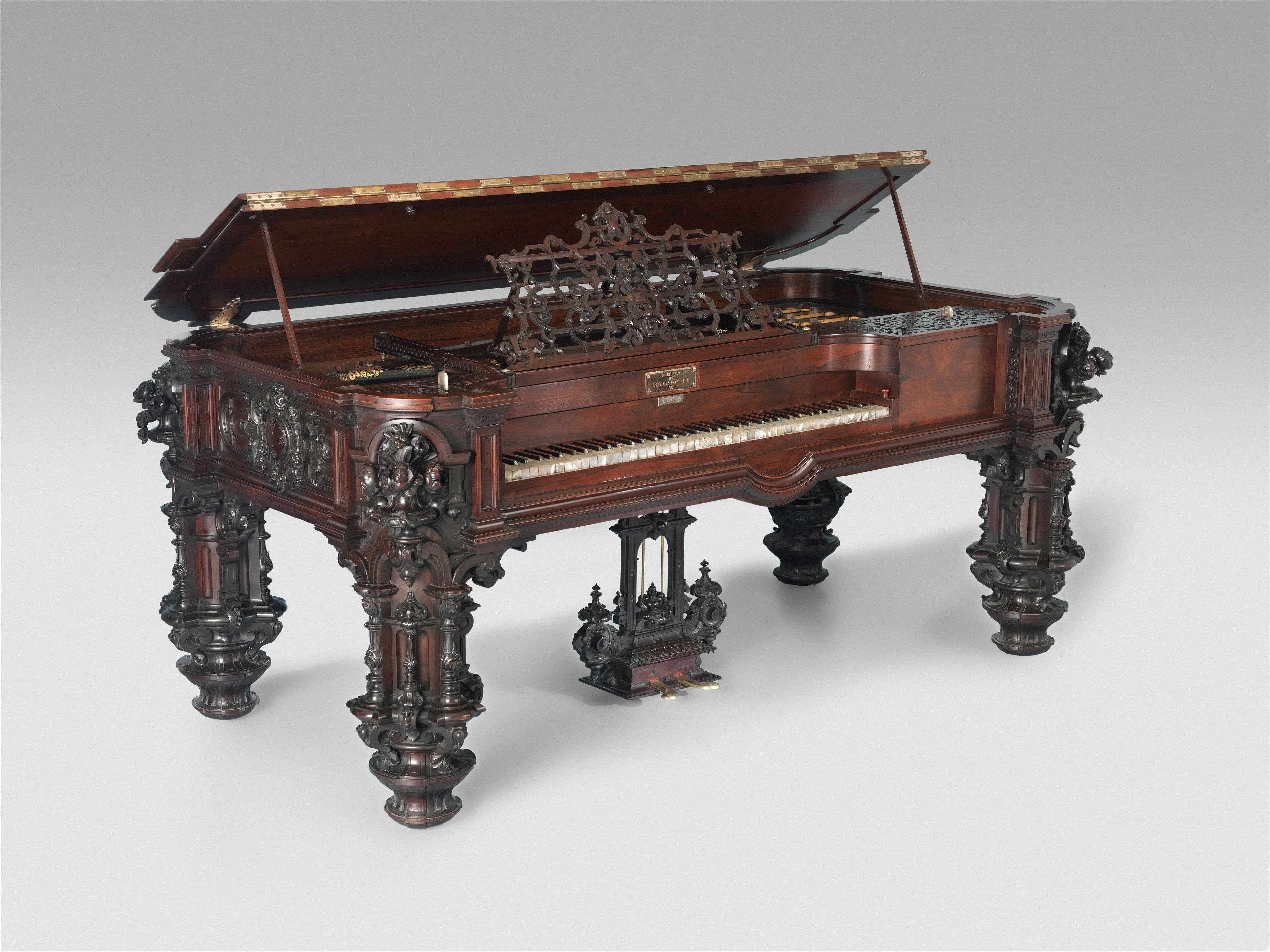 An ornate dark wood grand piano with intricate carvings and a raised lid