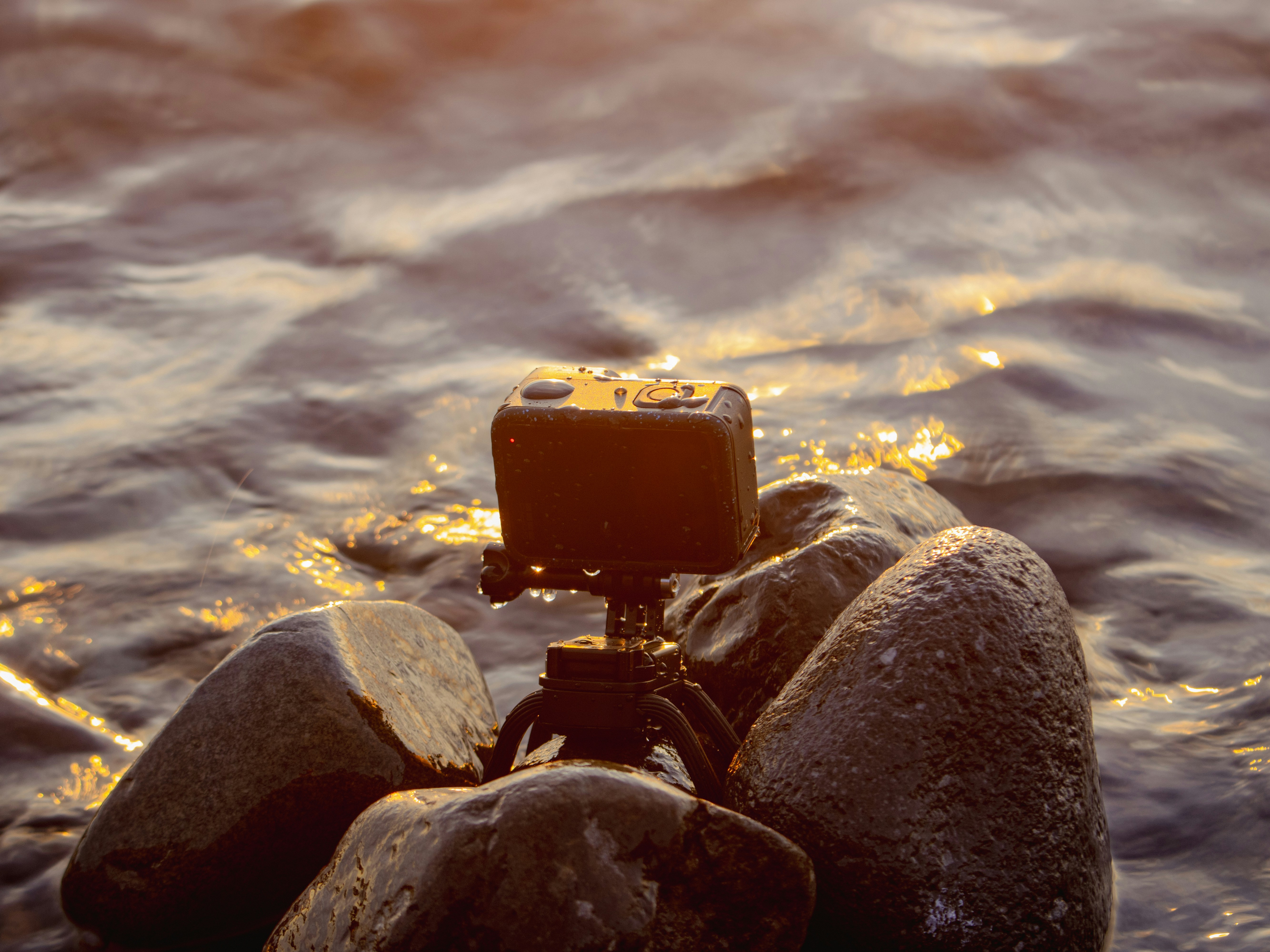 An action camera on a small tripod among wet rocks in flowing water