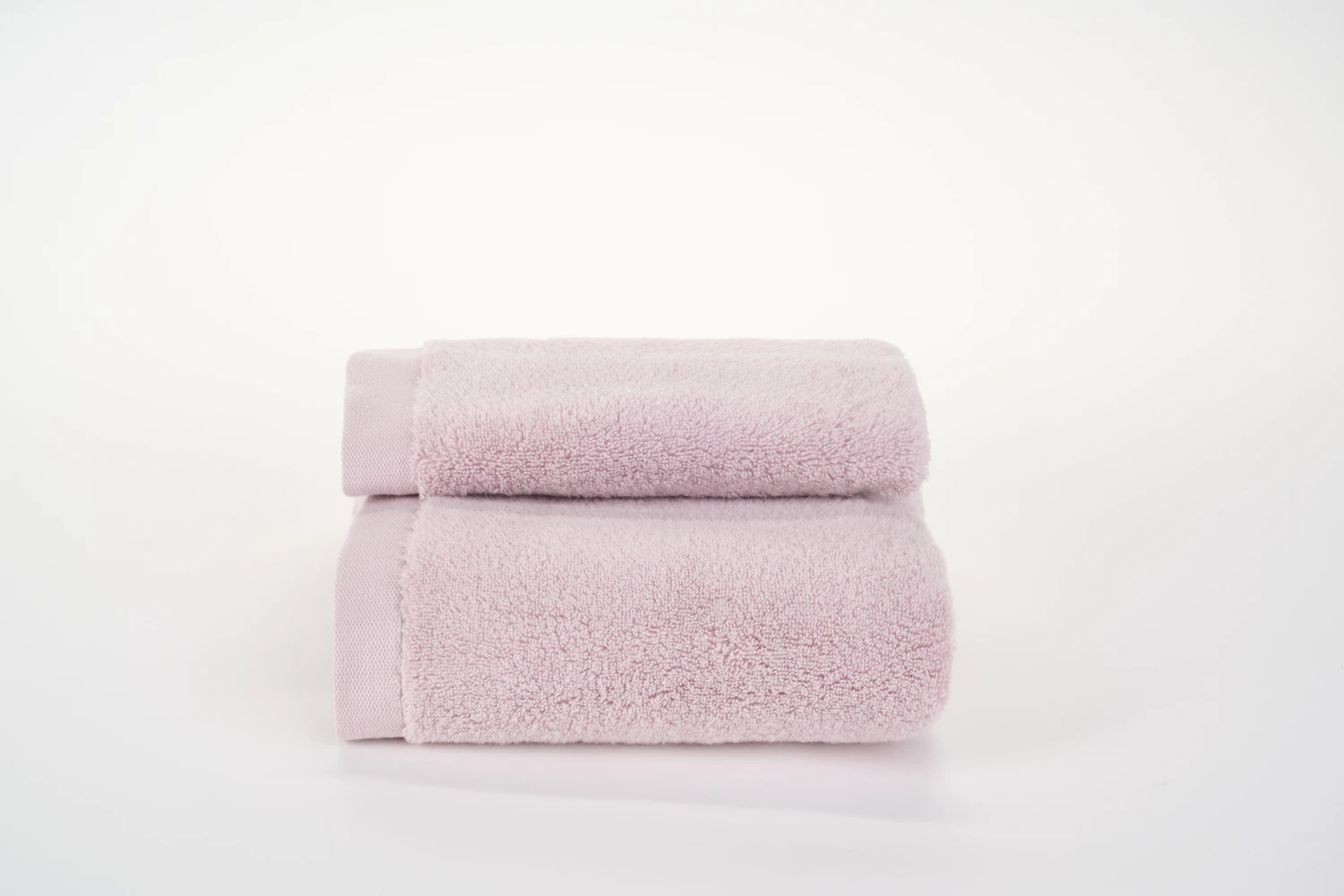 Two folded pale pink towels squared off on a white shelf