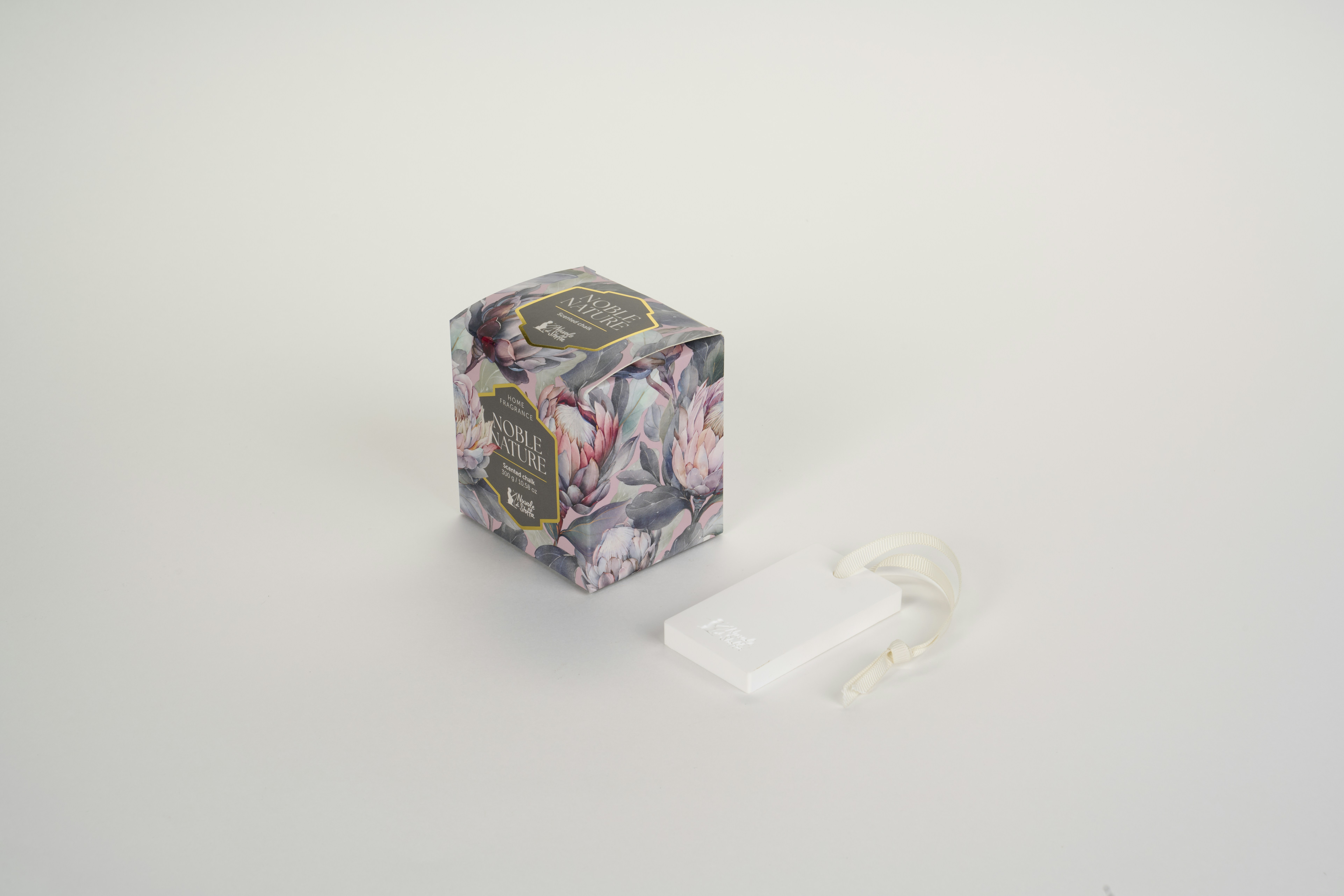 A floral patterned box and a white ceramic fragrance tag on a white surface
