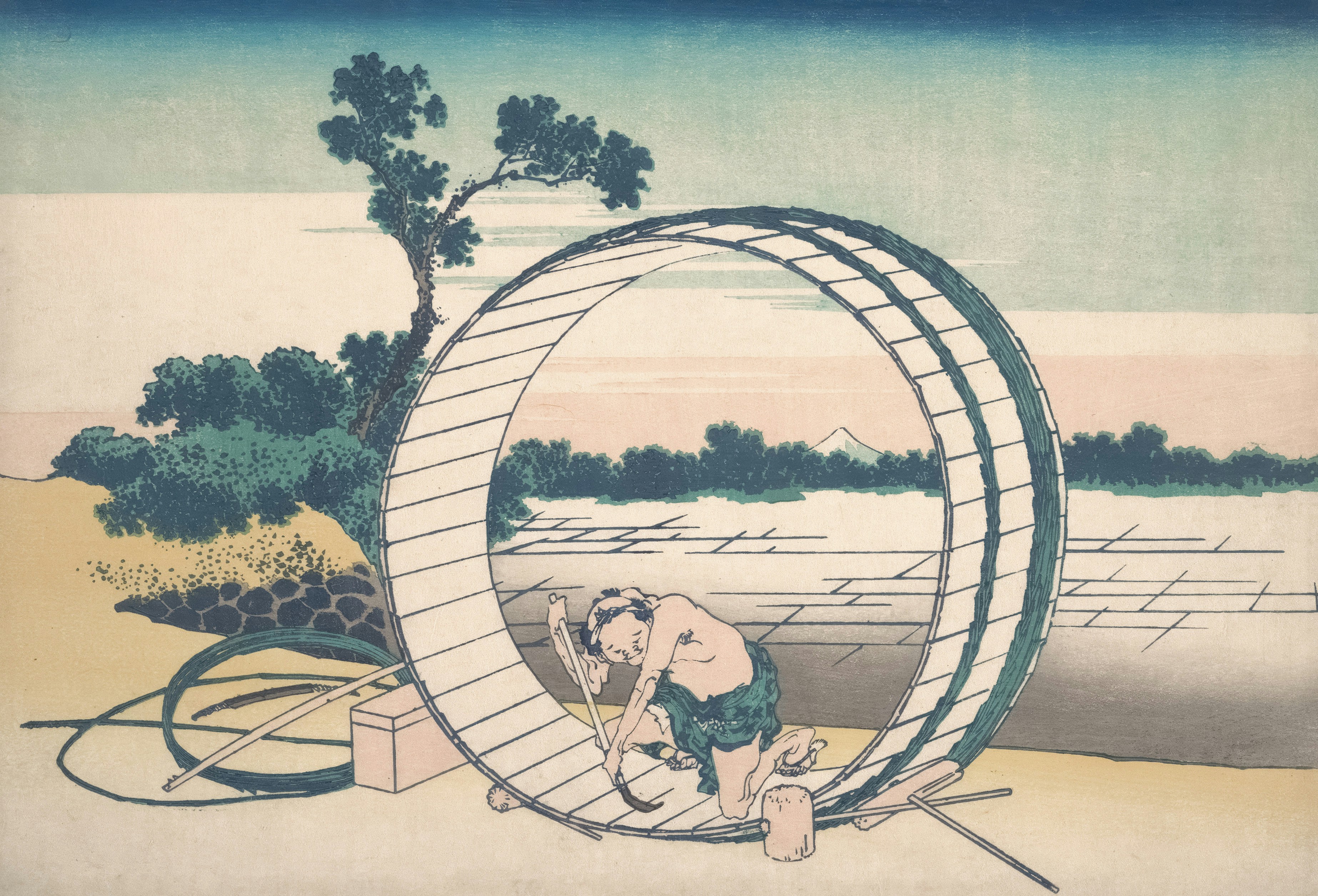 A person kneeling inside a large wooden barrel frame on a riverbank
